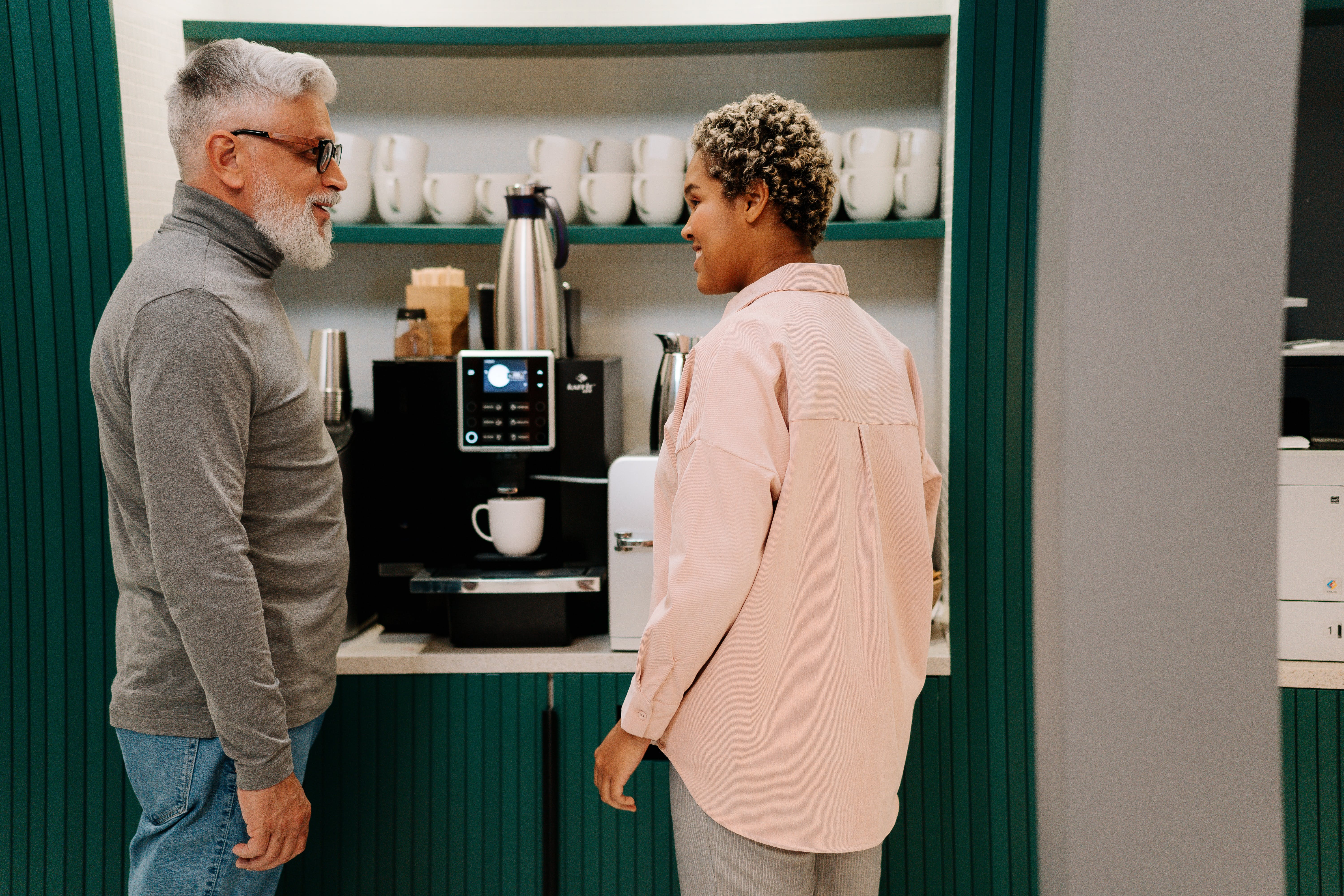 Un hombre mayor hablando con una mujer más joven delante de una máquina de café | Fuente: Pexels