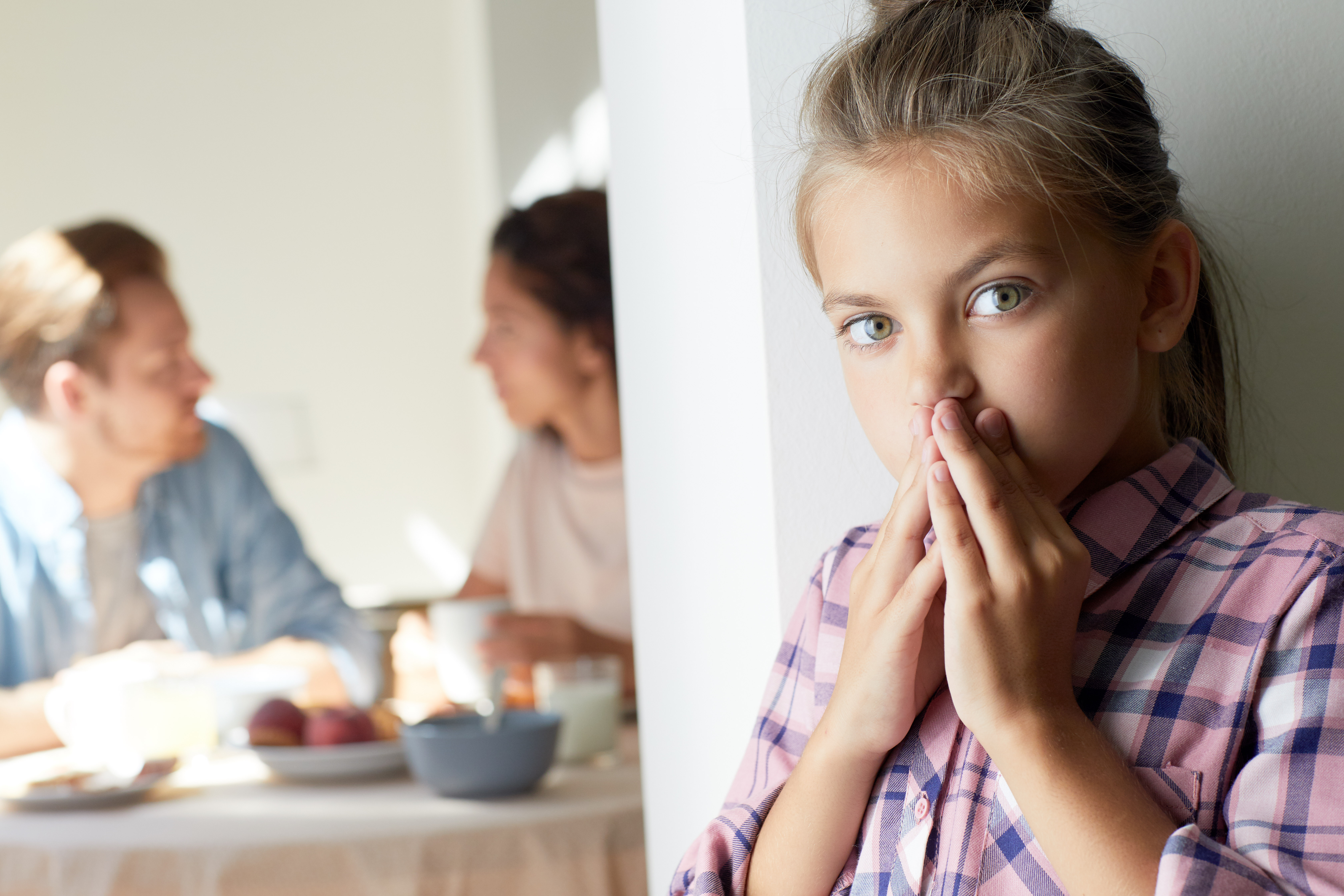 Niña detrás de una puerta mientras un hombre y una mujer hablan dentro | Foto: Shutterstock