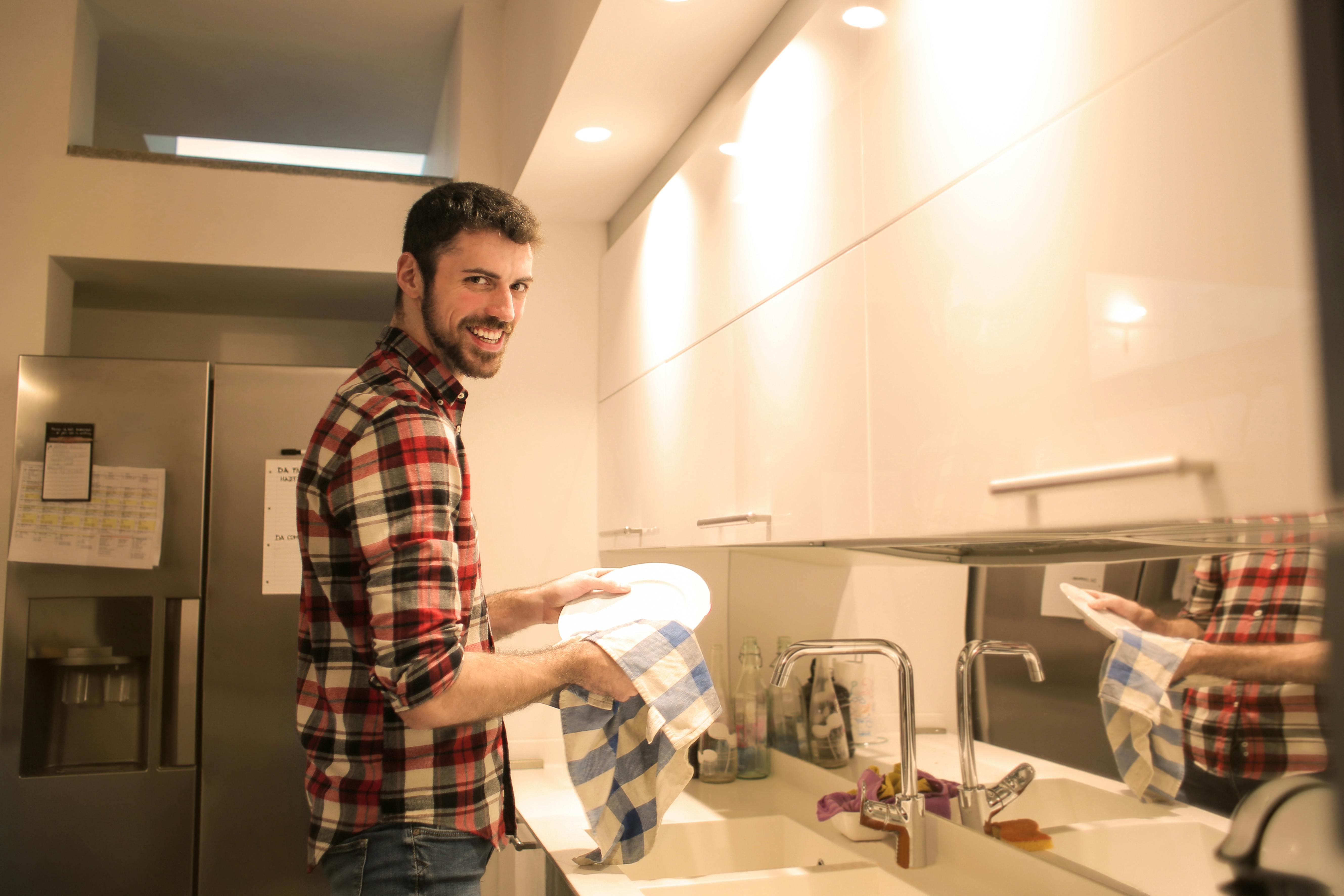 Hombre sonriendo mientras friega los platos | Fuente: Pexels