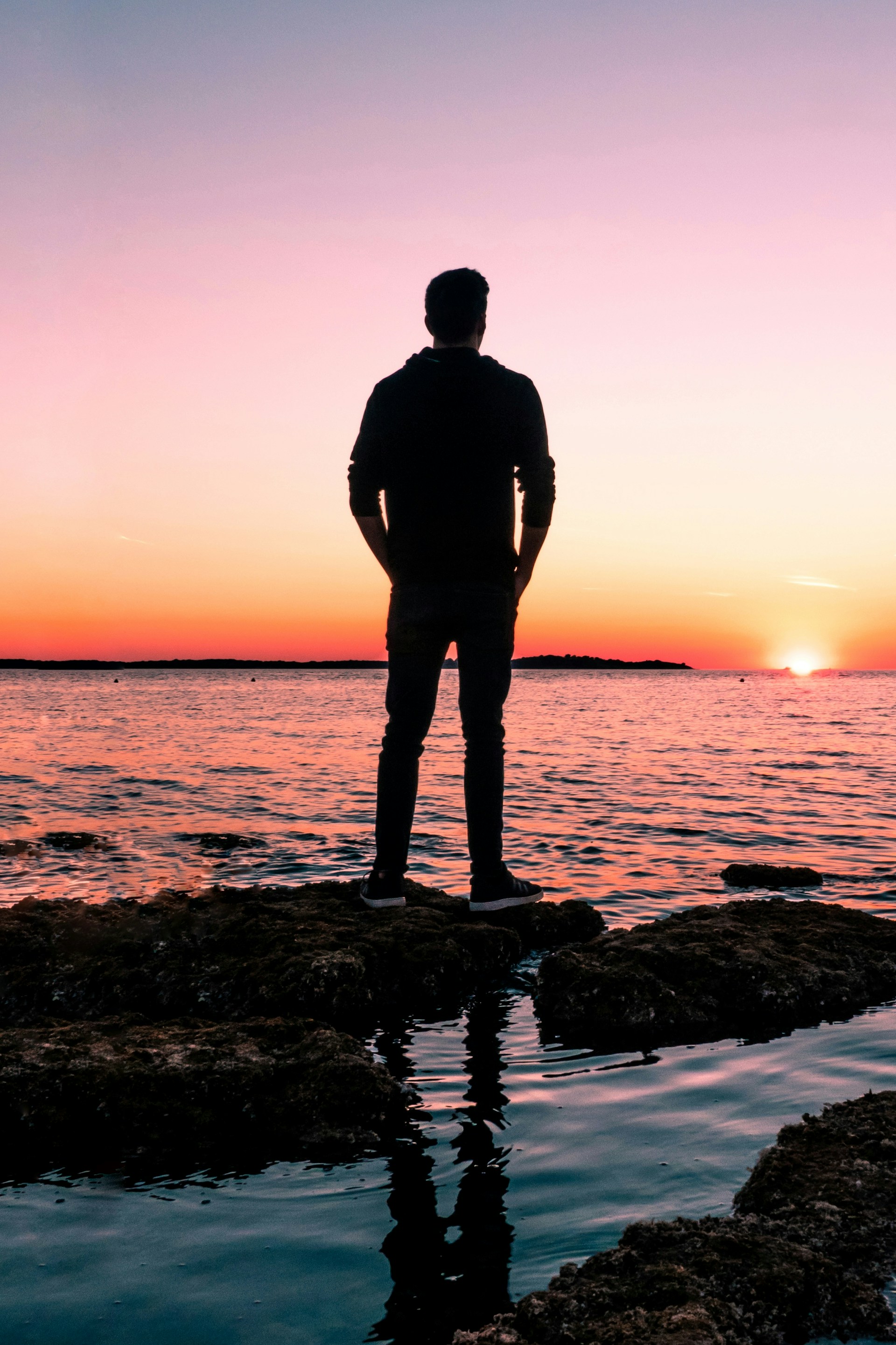 Un hombre observa la luz dorada del sol desde la orilla en un atardecer pintoresco | Fuente: Unsplash