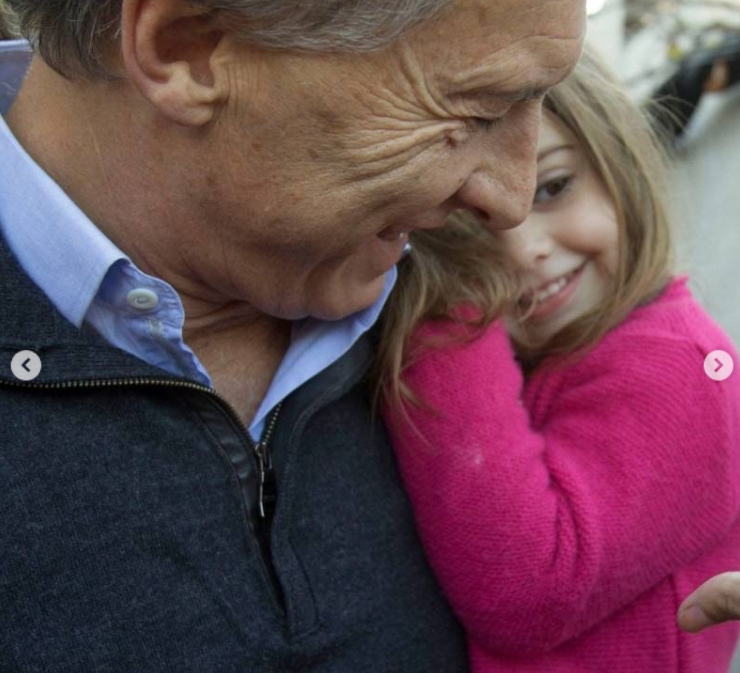 Mauricio Macri sonríe cálidamente mientras sostiene en brazos a Antonia, quien viste un suéter tejido de color fucsia. La niña se apoya cariñosamente contra el pecho de su padre con una mirada pícara y alegre. | Fuente: Instagram/mauriciomacri