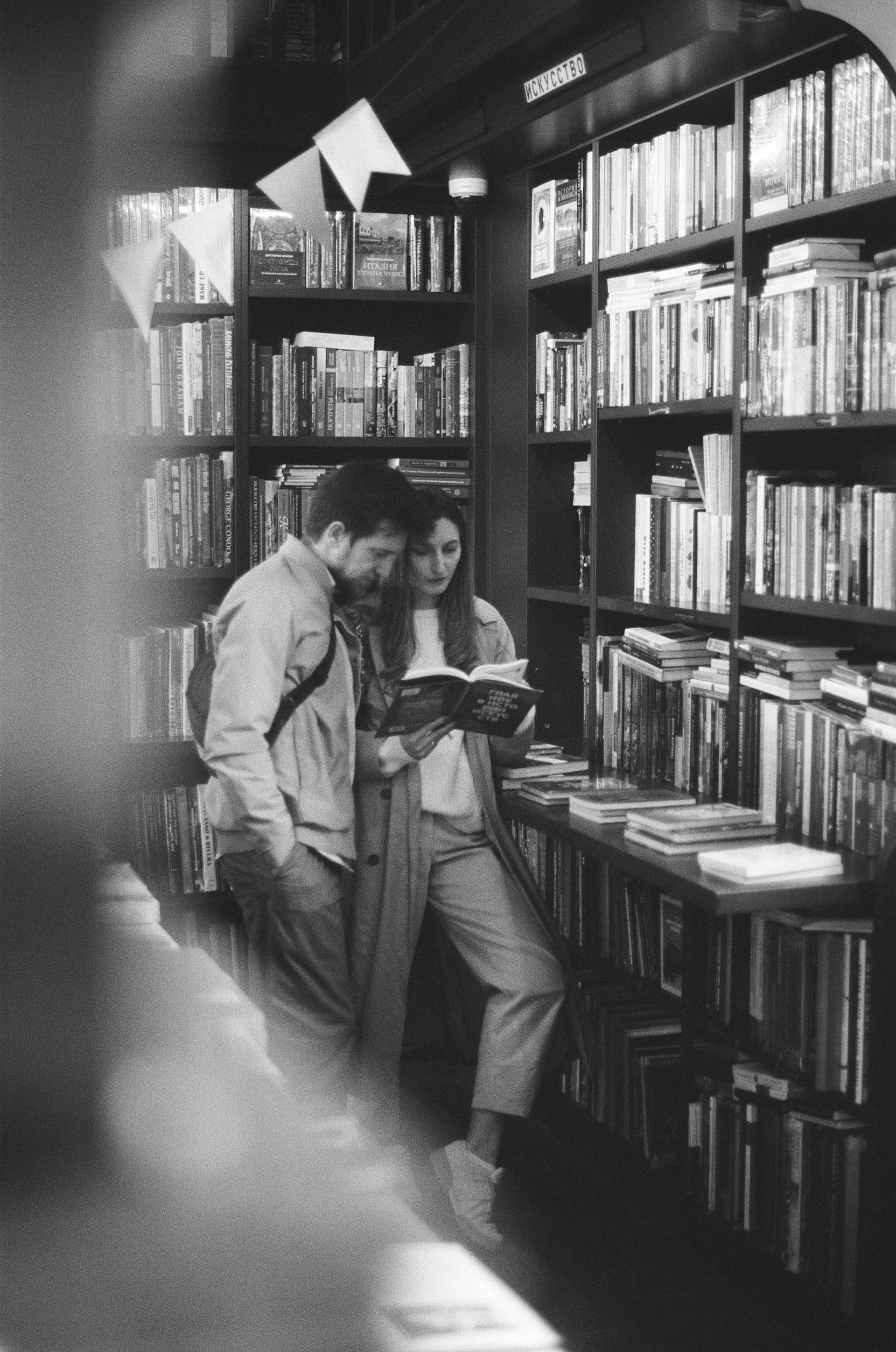 Foto en escala de grises de una pareja leyendo un libro en una biblioteca | Fuente: Pexels
