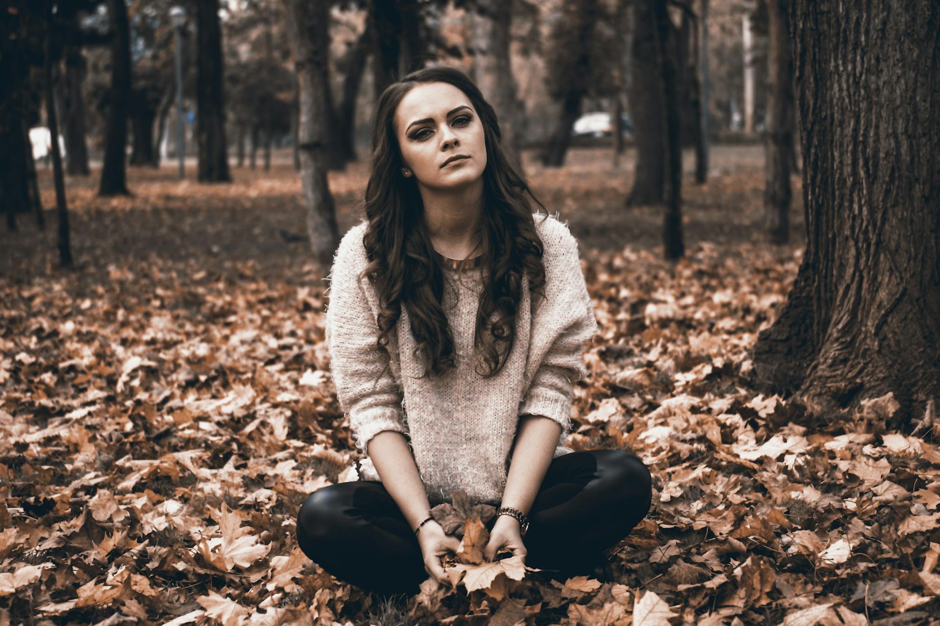 Una joven sentada en un bosque sujetando hojas caídas | Foto: Pexels