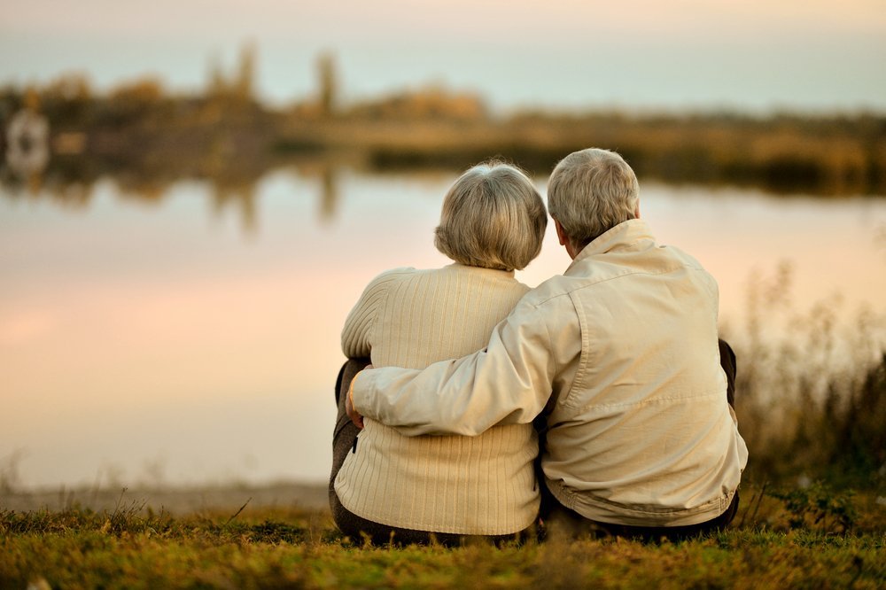 Feliz pareja de ancianos sentada en verano cerca del lago durante el atardecer. | Fuente: Shutterstock