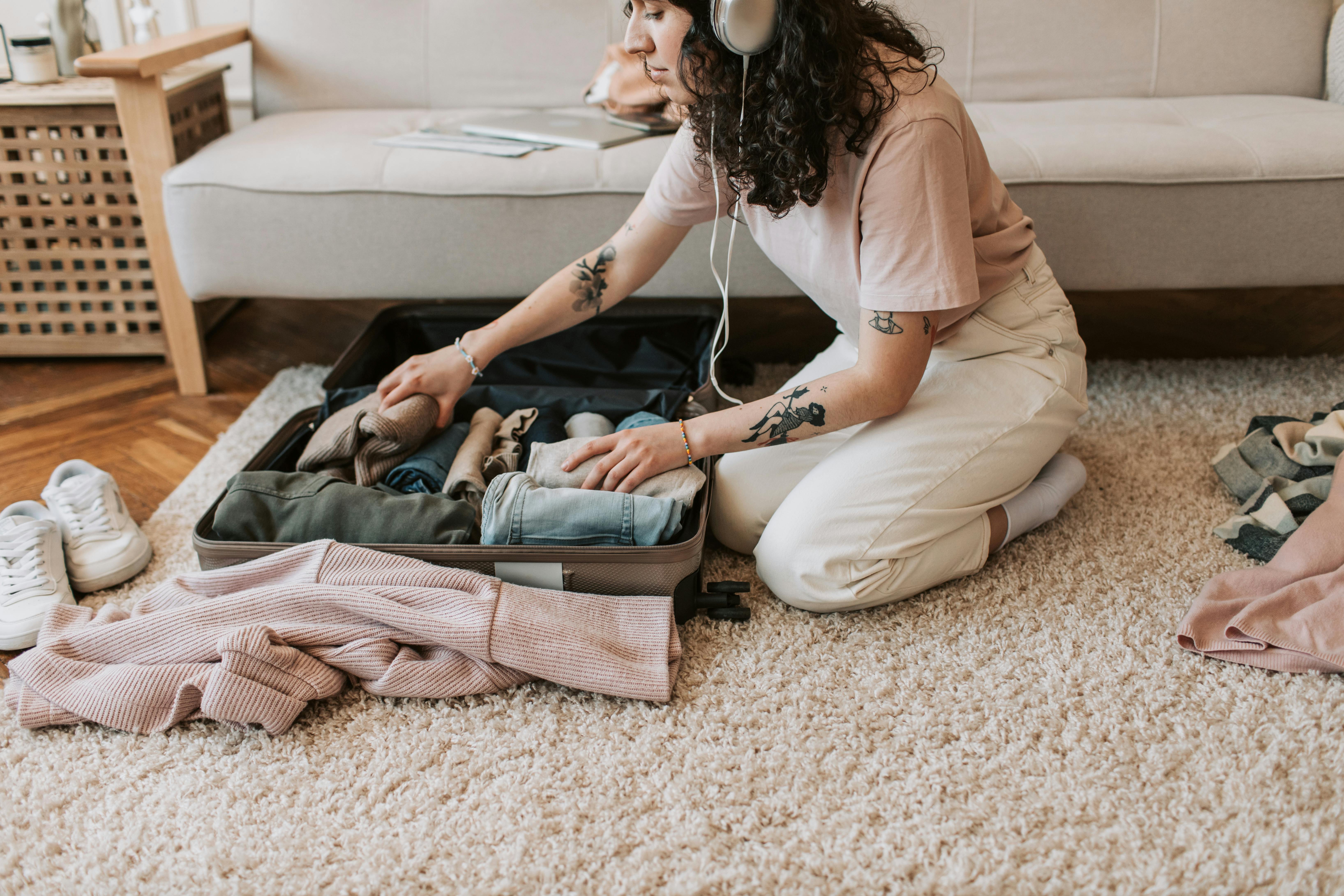 Una mujer empaquetando su ropa mientras lleva auriculares | Fuente: Pexels