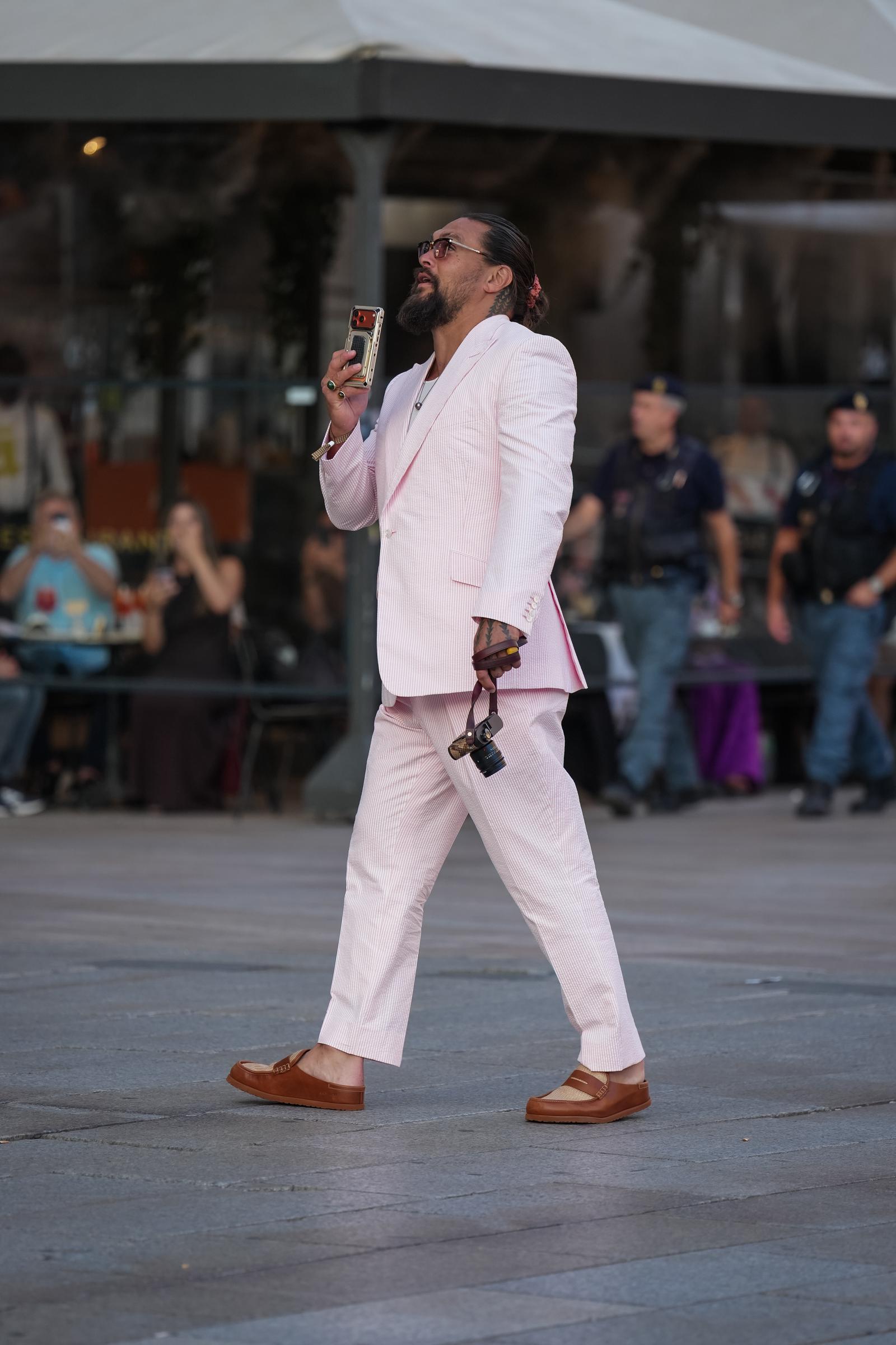 Momoa sale a la calle con el móvil en la mano, dejando ver las líneas holgadas del traje y sus zapatos marrones sin cordones. | Fuente: Getty Images