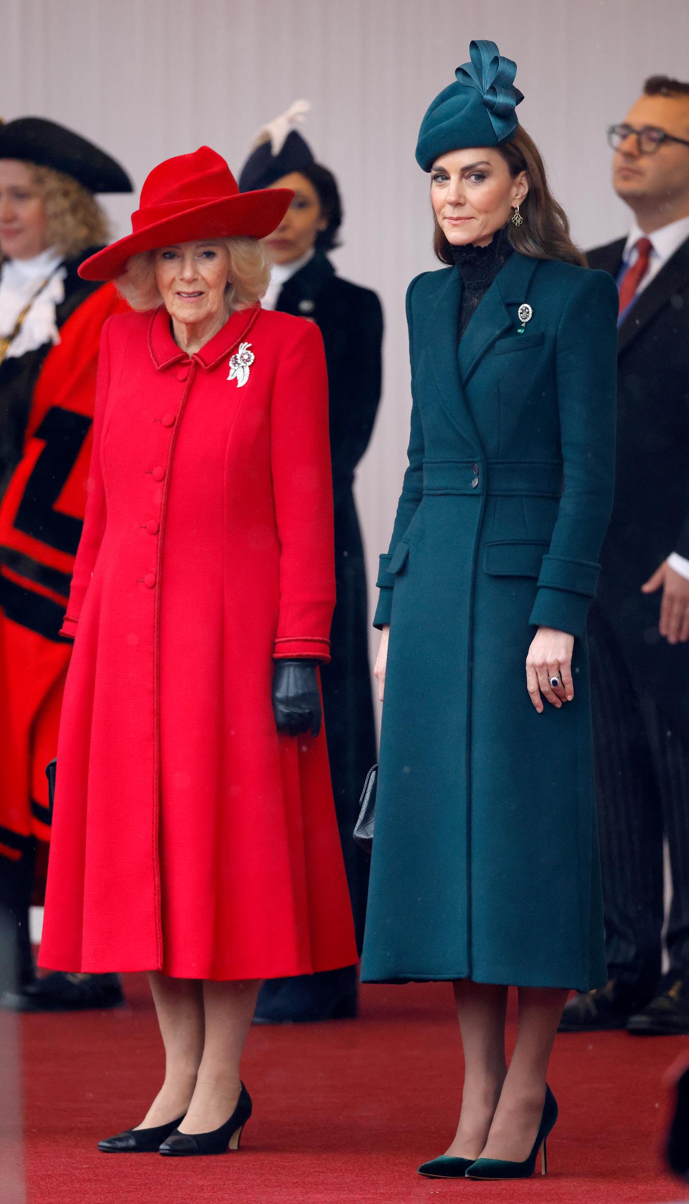 Catherine, princesa de Gales, posa en la alfombra roja junto a la reina Camilla en Windsor el 20 de octubre de 2026. En un llamativo contraste con el abrigo acampanado de color rojo vivo de Camilla y su sombrero de ala ancha a juego, Catherine luce un vestido-abrigo midi de color verde esmeralda con hombros marcados y estructurados, combinado con un tocado esculpido a juego, detalles de encaje negro en el escote y zapatos de tacón de punta de terciopelo verde. | Fuente: Getty Images