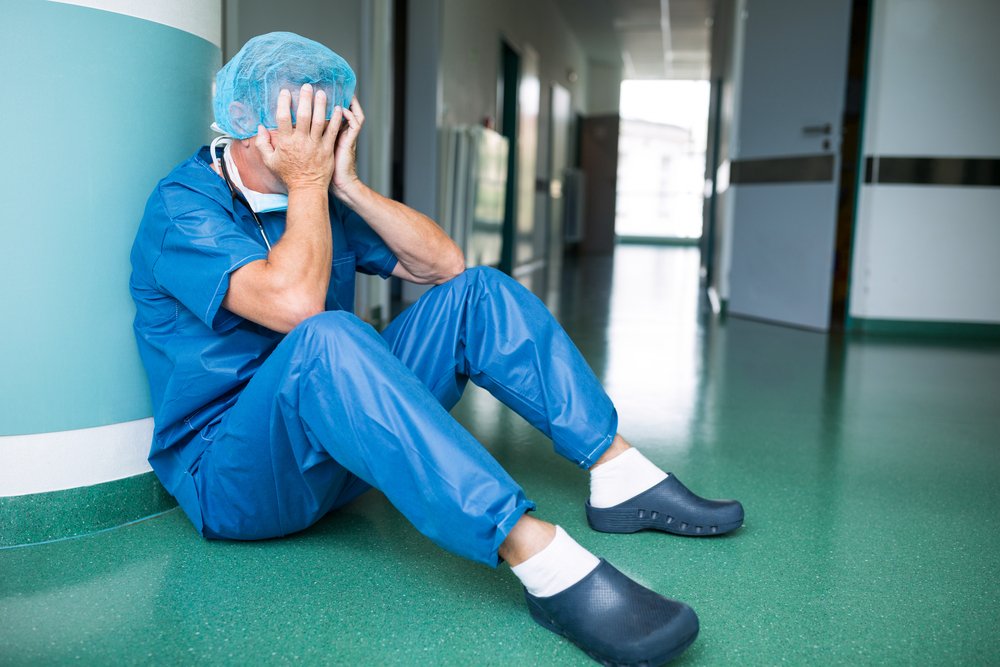 Médico afligido sentado en el suelo en el pasillo de un hospital. | Foto: Shutterstock