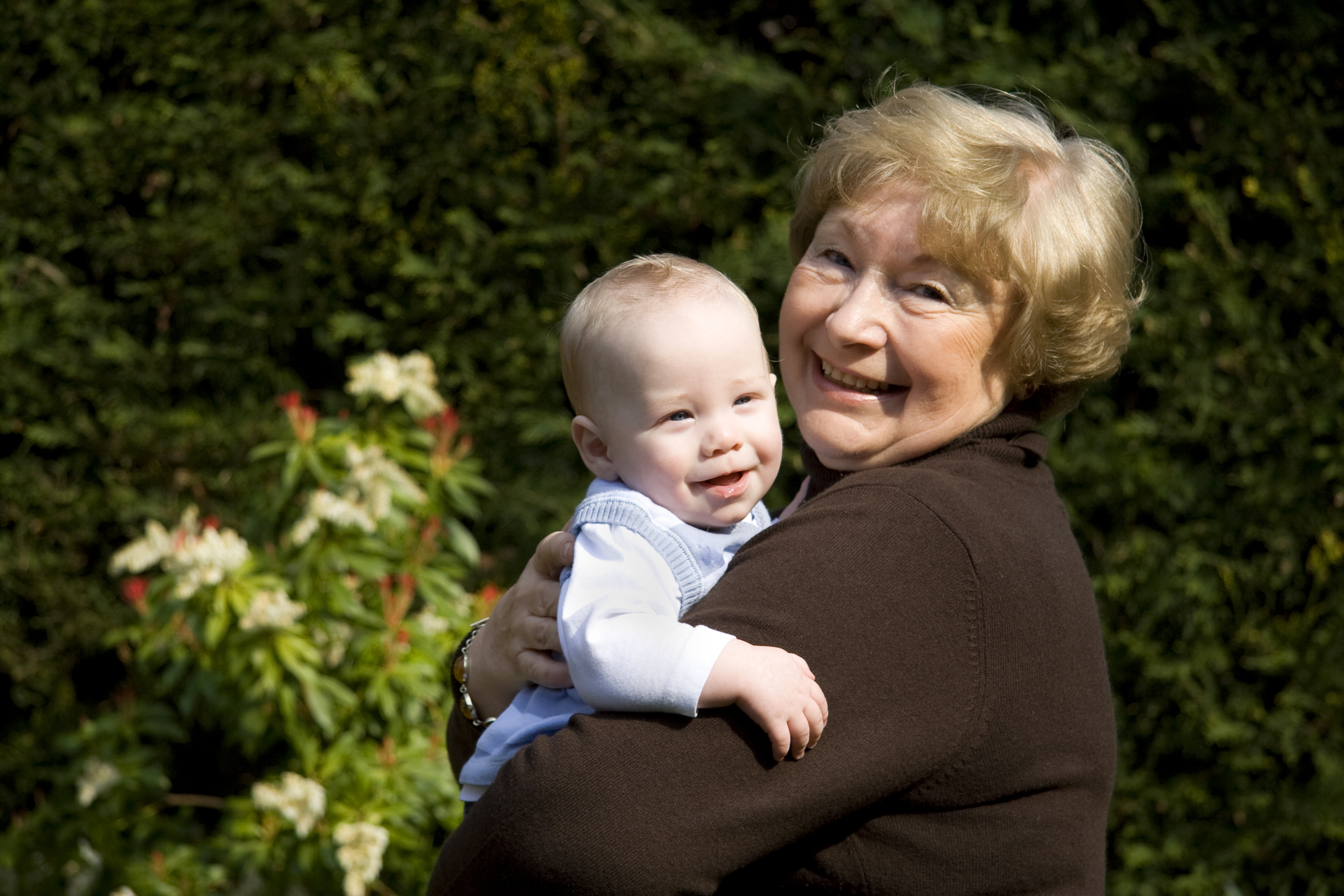 Una mujer mayor sonríe mientras acurruca a un bebé feliz. | Foto: Shutterstock