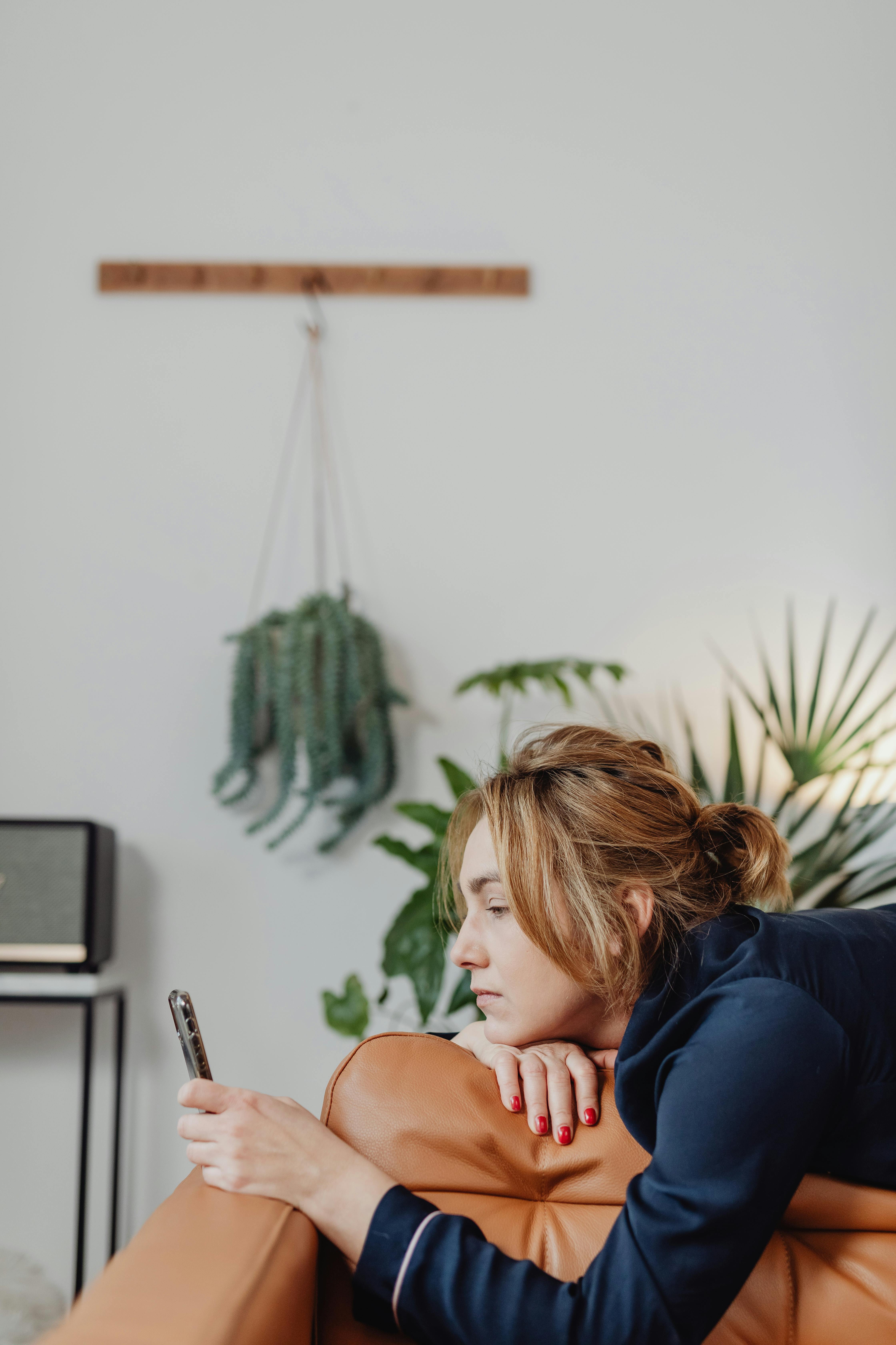 Mujer tumbada en un sofá de cuero marrón mirando su móvil | Fuente: Pexels