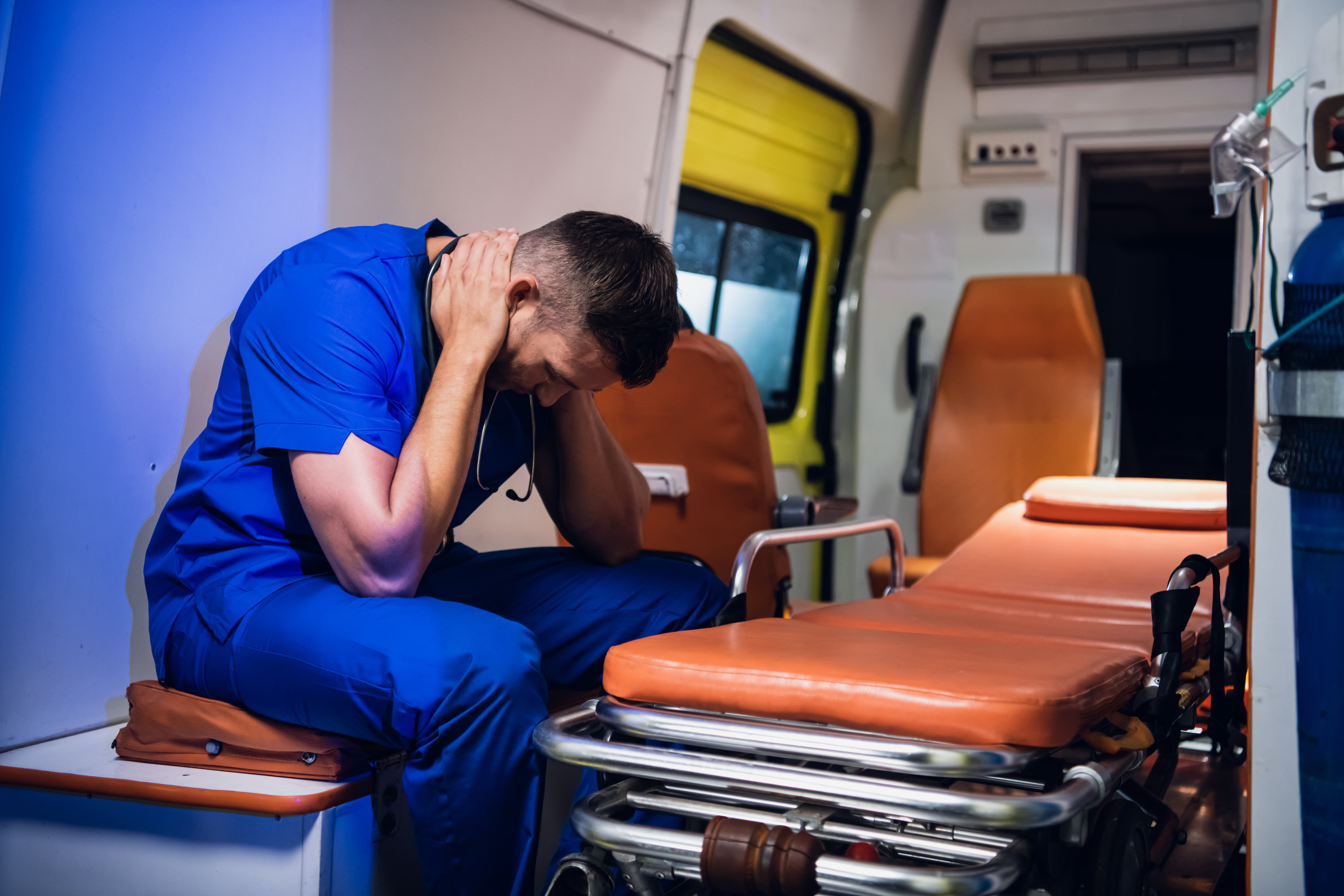Un paramédico exhausto se toma un pequeño descanso sentado en una ambulancia con las manos alrededor del cuello. | Foto: Shutterstock