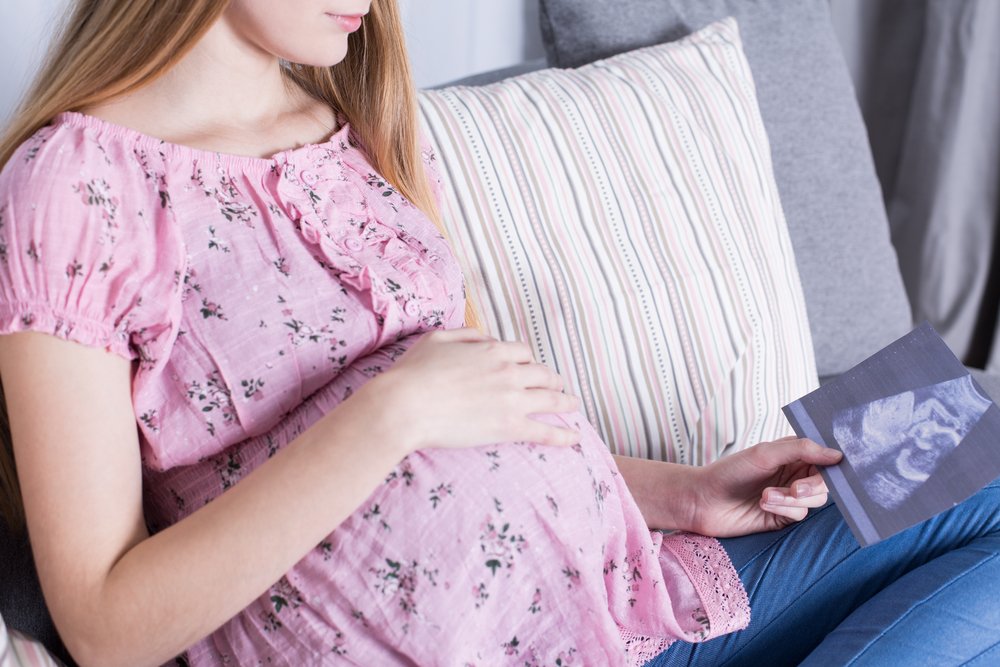 Imagen recortada de una mujer joven mirando una imagen de USG de su bebé| Foto: Shutterstock