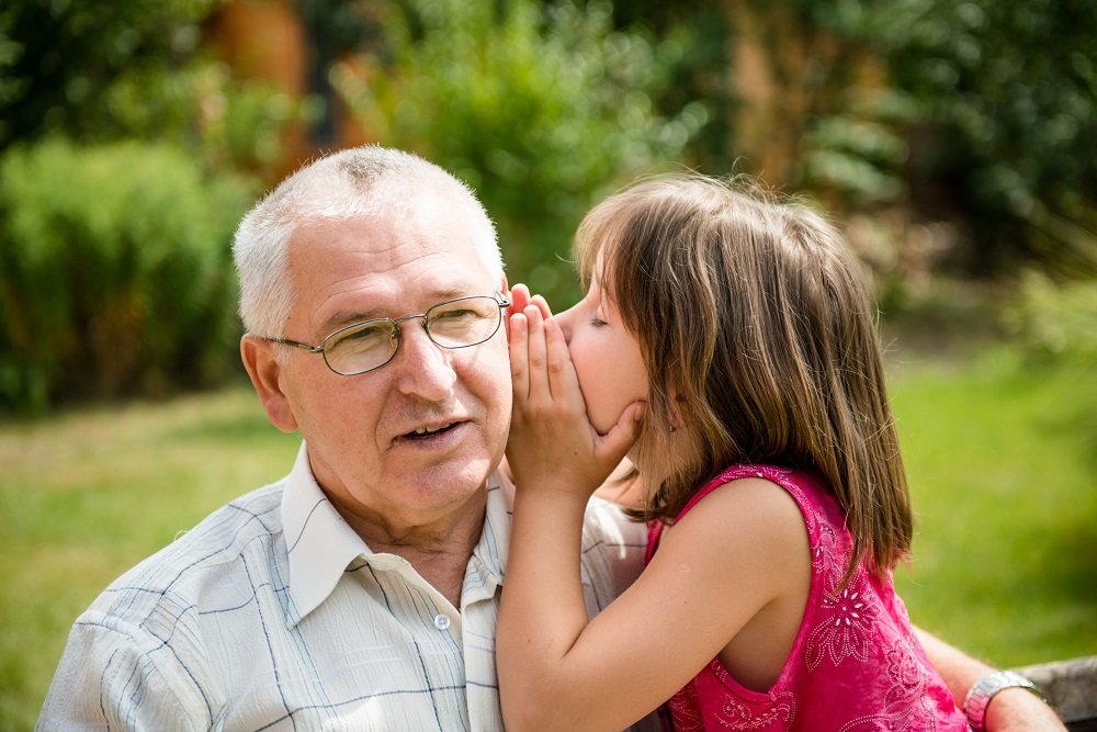 Una niña le dice un secreto a su abuelo. Fuente: Shutterstock
