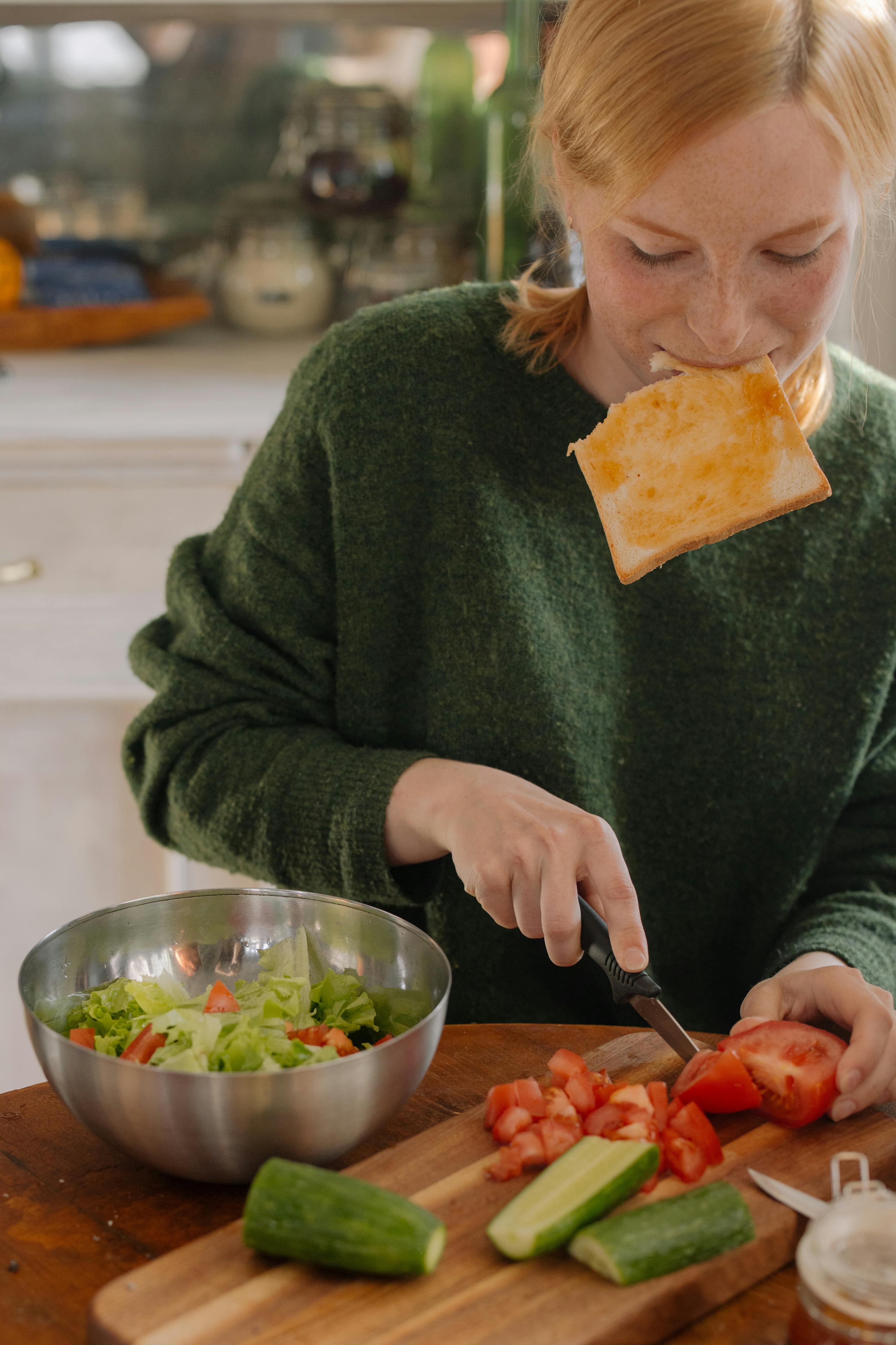 Una mujer comiendo y cortando verduras | Fuente: Pexels