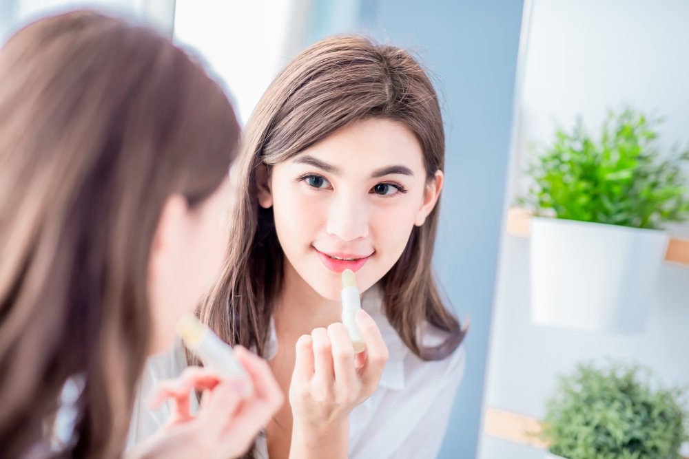 Mujer aplicando labial humectante en sus labios frente a un espejo. | Foto: Shutterstock