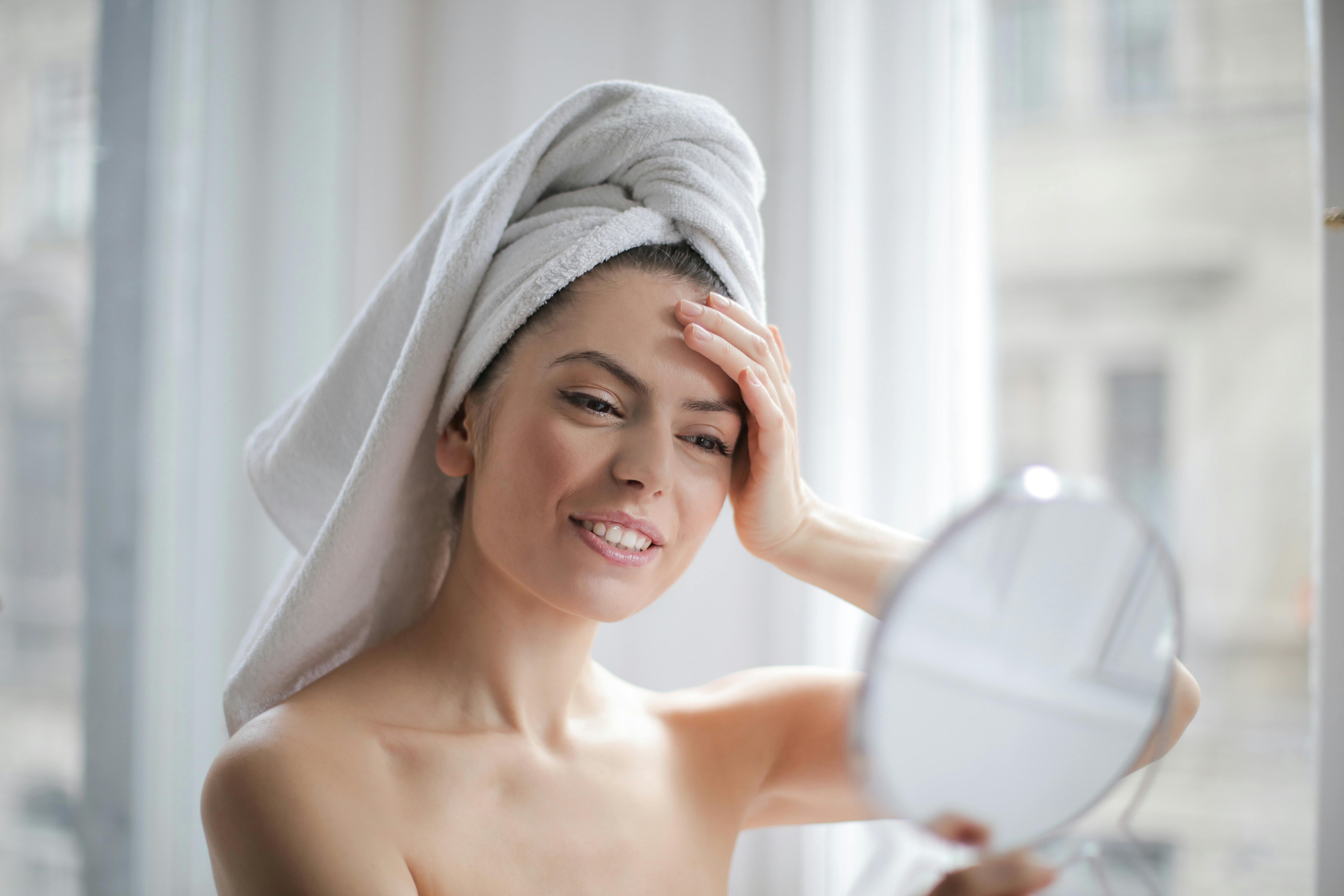 Una mujer feliz mirándose al espejo mientras se seca el pelo con una toalla | Fuente: Pexels