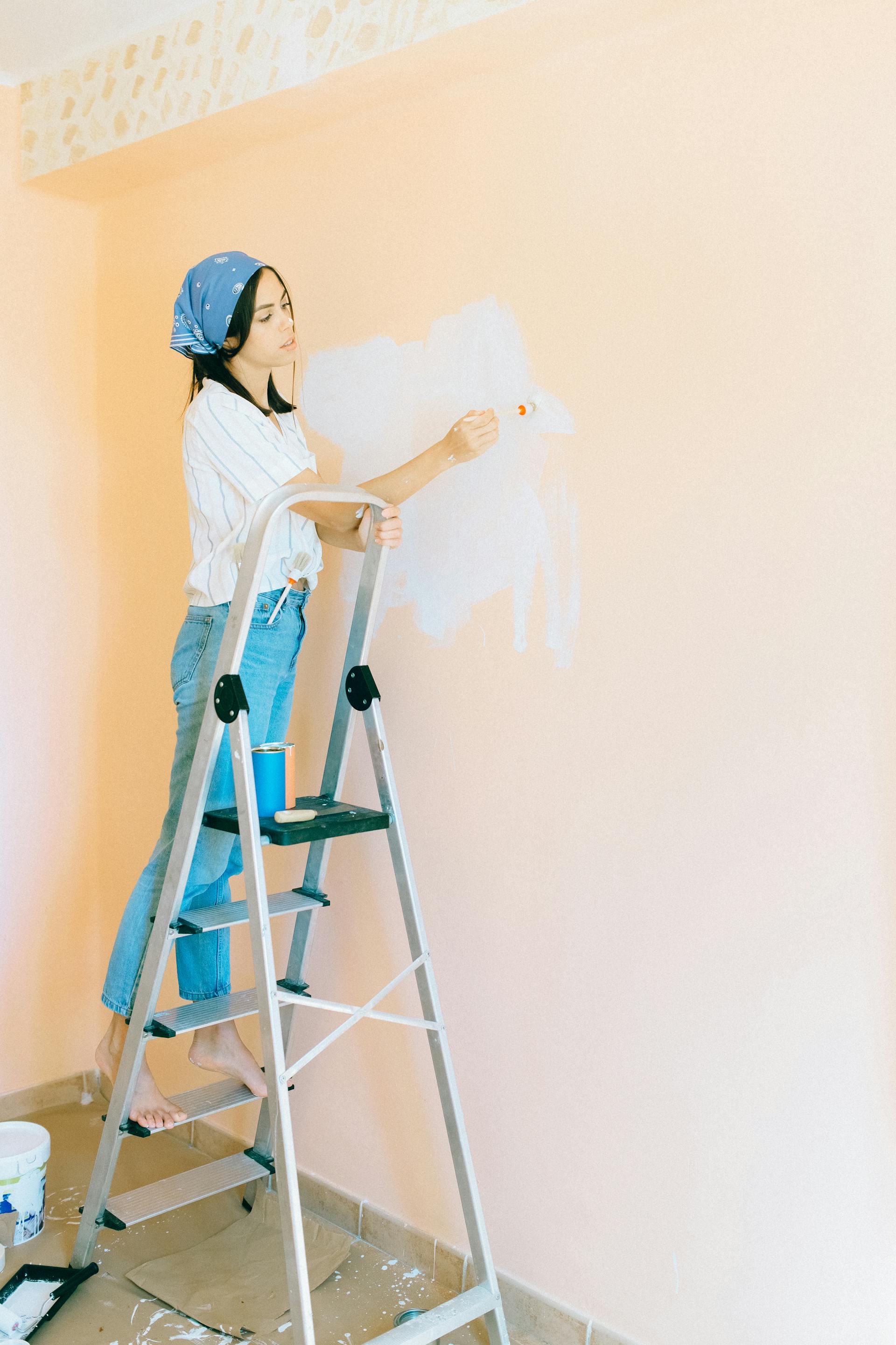 Una mujer de pie sobre una escalera de mano y pintando una pared | Fuente: Pexels