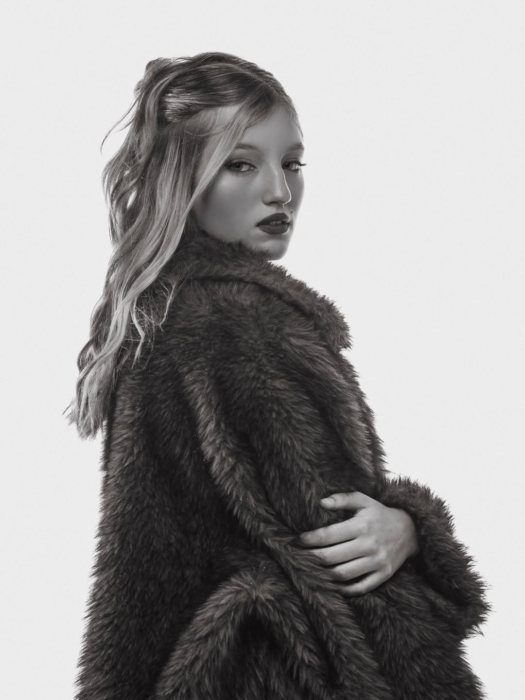 Allegra Cubero posa de perfil con abrigo de piel, mirada hacia la cámara, en imagen en blanco y negro.