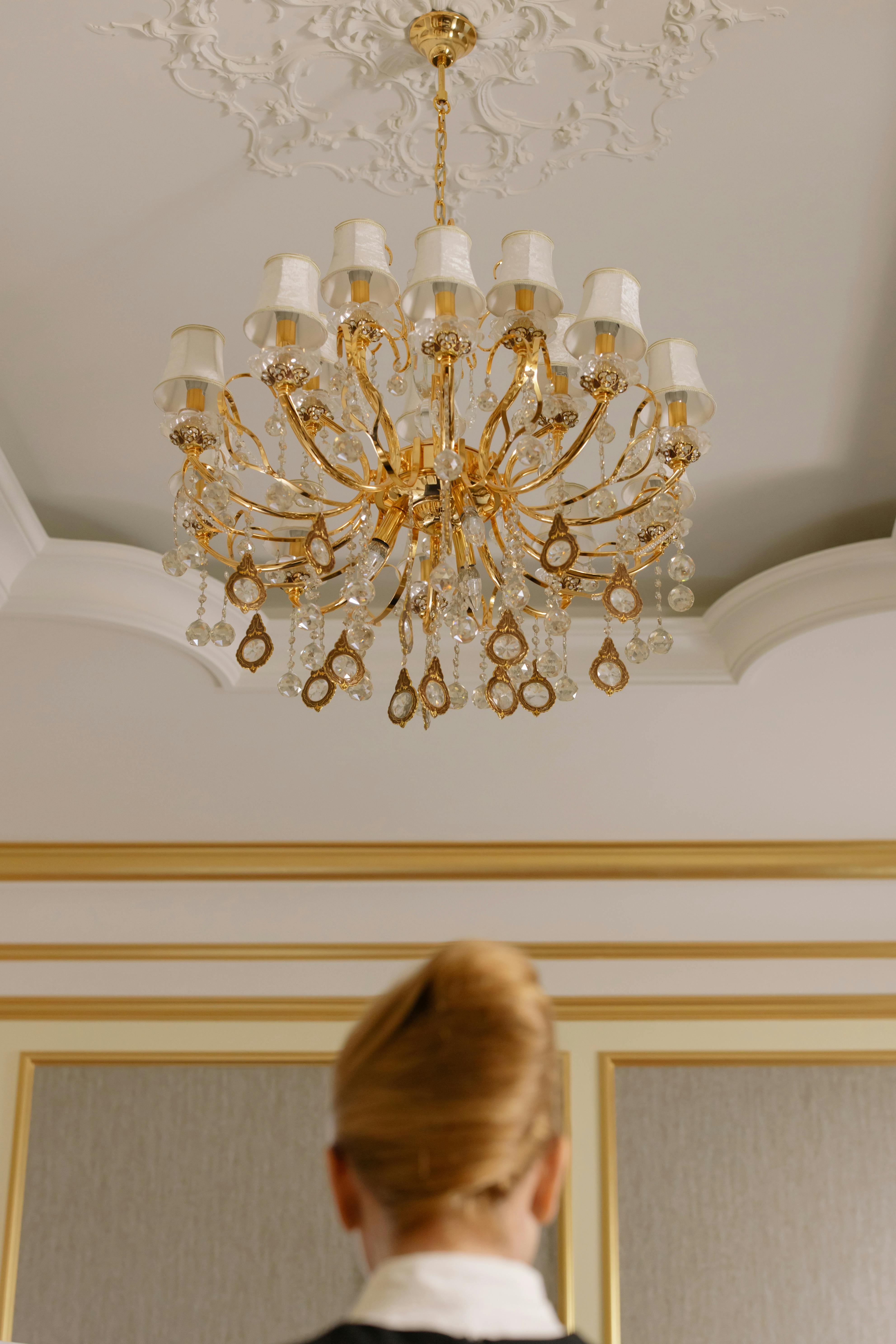 Mujer de pie bajo la lámpara de araña de una habitación de hotel | Fuente: Pexels