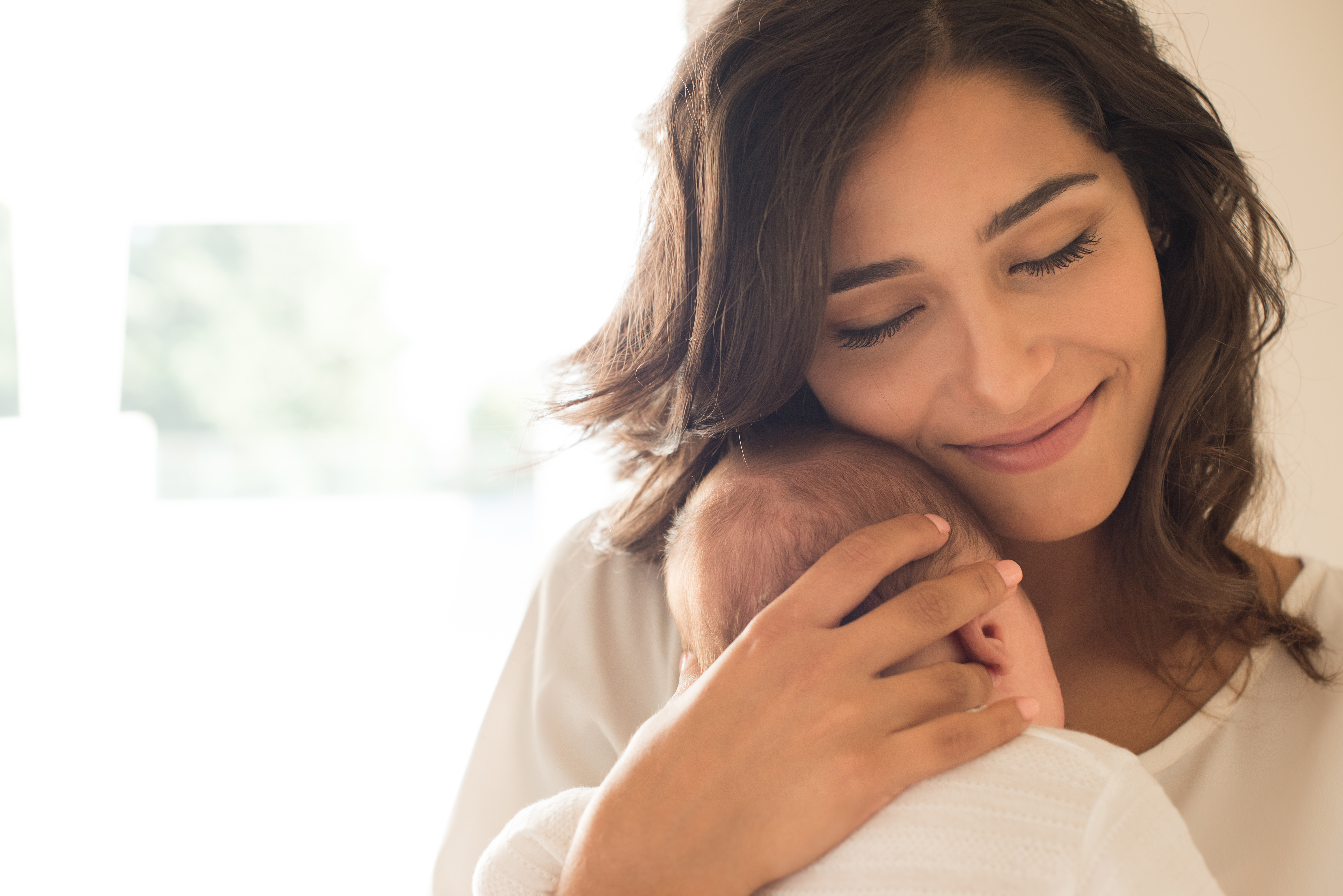 Una madre sonríe mientras acurruca a su bebé contra su pecho. | Foto: Shutterstock