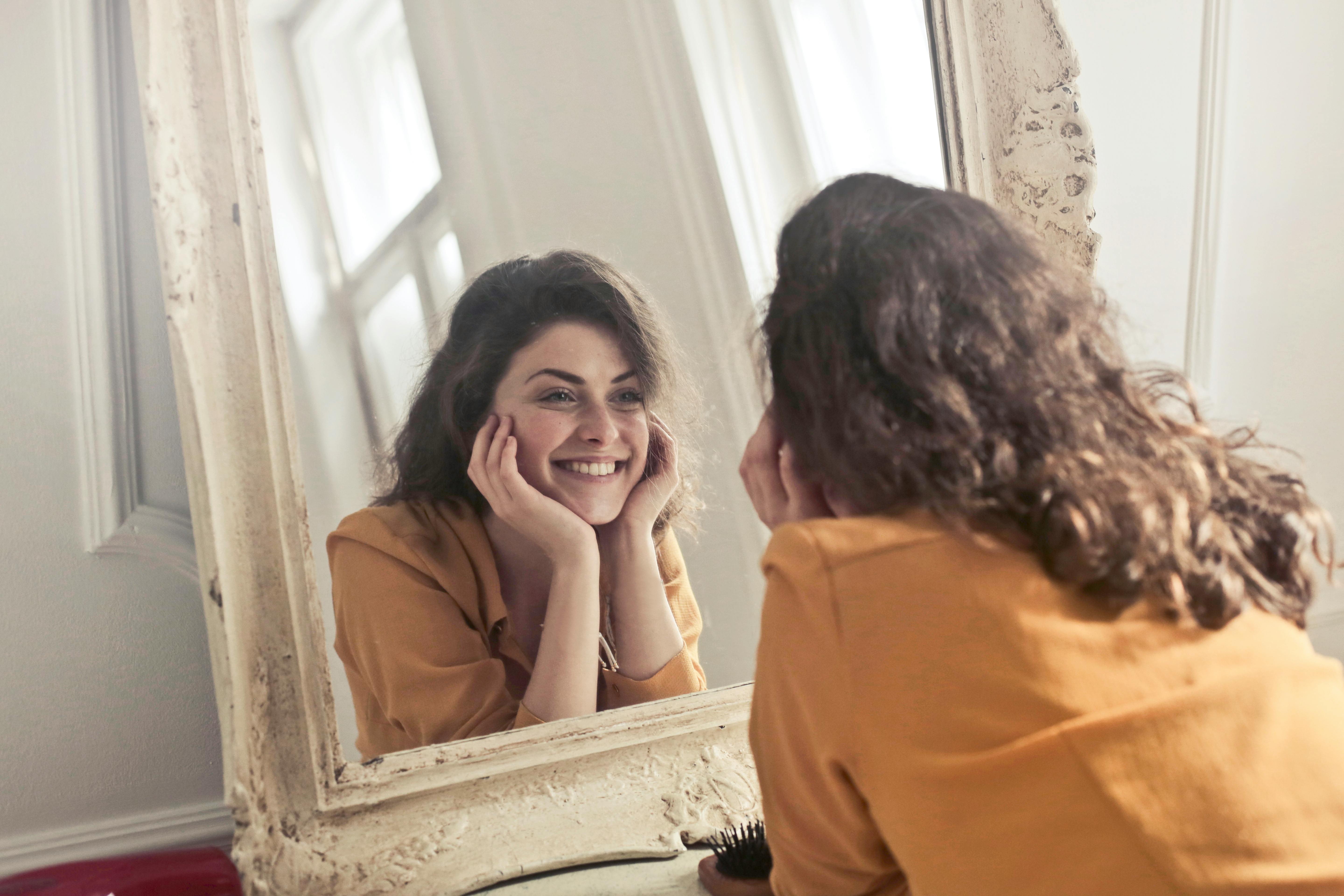 Mujer sonriendo mientras se mira al espejo | Fuente: Pexels