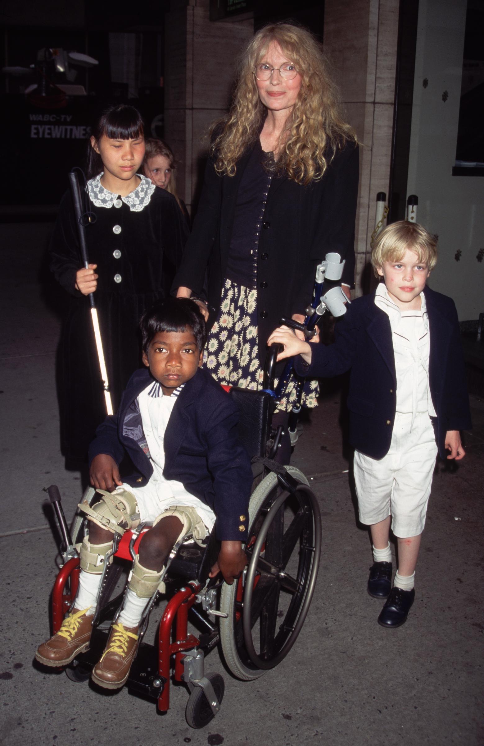 Mia Farrow con sus hijos, junto a Tam Farrow en silla de ruedas mientras pasean por el Lincoln Center en el estreno de "Anne Frank Remembered" en Nueva York en 1995. | Fuente: Getty Images