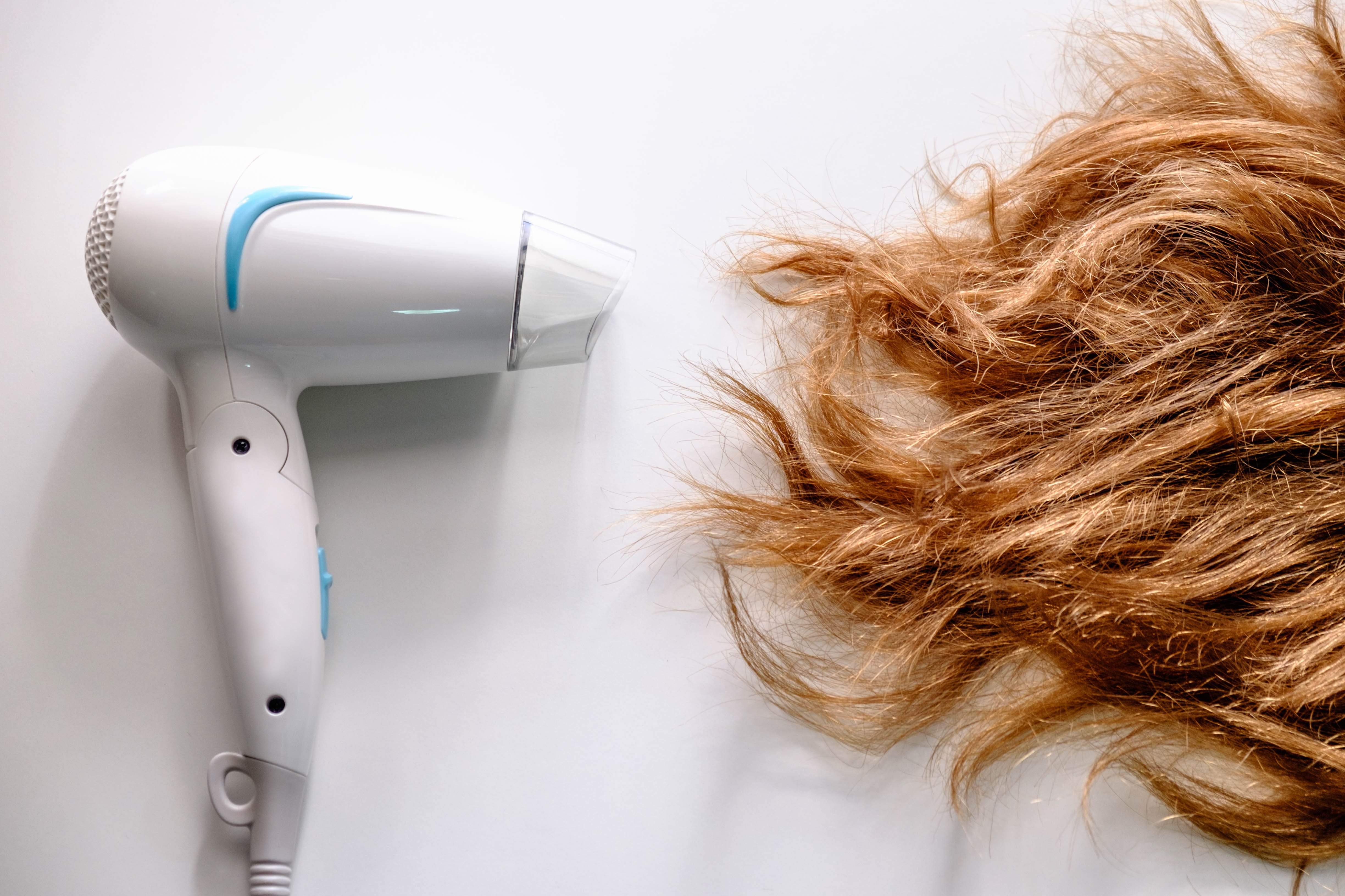 Secador de pelo junto a cabello rubio dañado. | Foto: Shutterstock