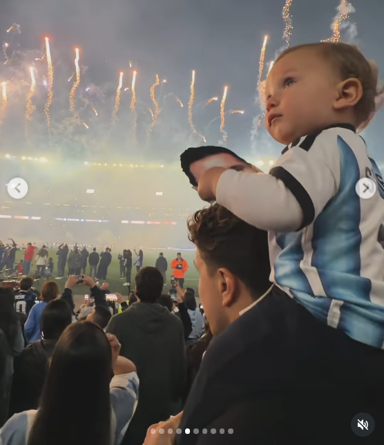 Faustino observó con atención y asombro el espectáculo de fuegos artificiales elevándose sobre la cancha desde los hombros de su padre. El bebé, vestido con la camiseta a bastones celestes y blancos, vivió el emotivo homenaje rodeado por la efervescencia de los hinchas que filmaban con sus celulares. | Fuente: Instagram/evabargiela