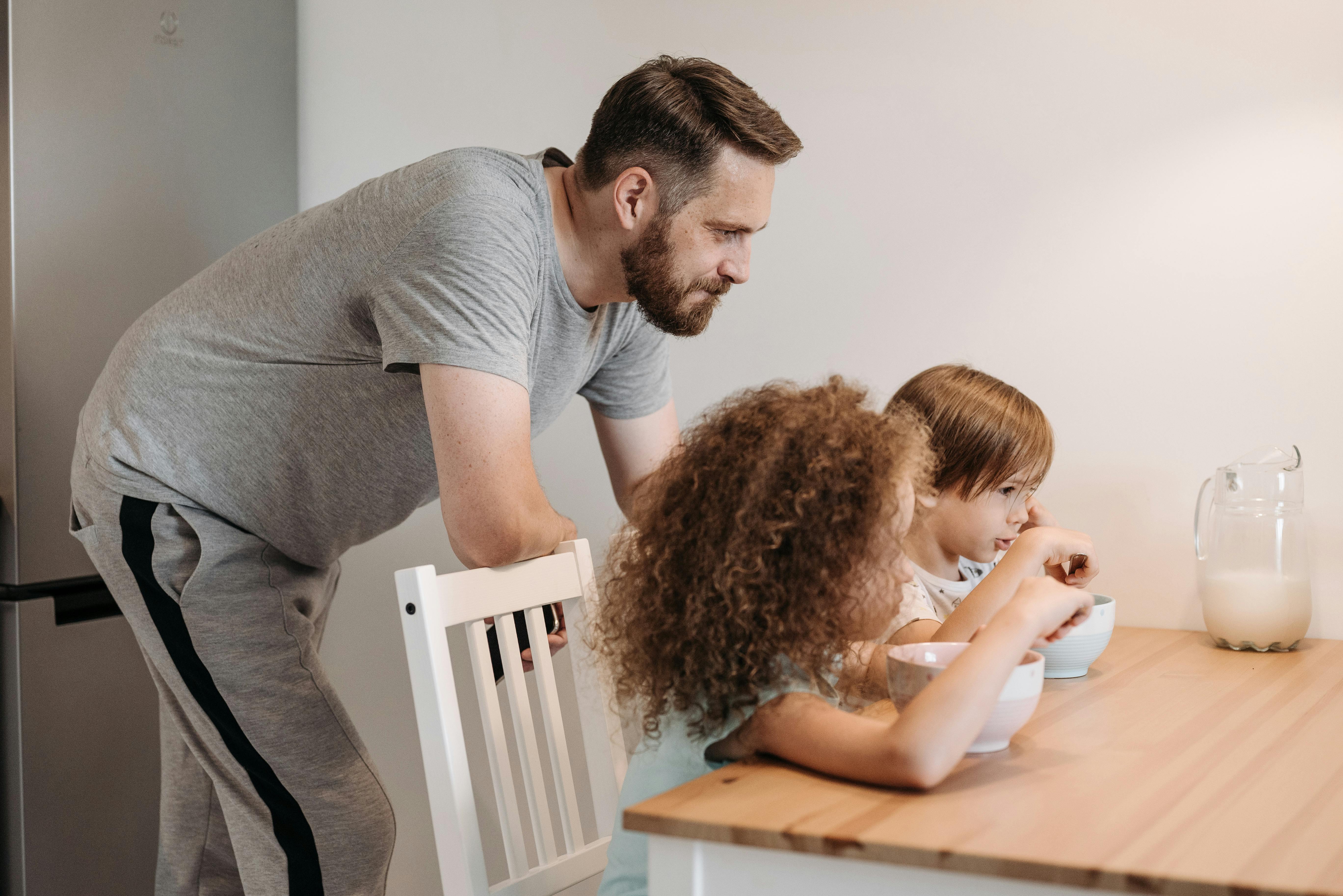 Un padre observando a sus dos hijas mientras desayunan | Fuente: Pexels