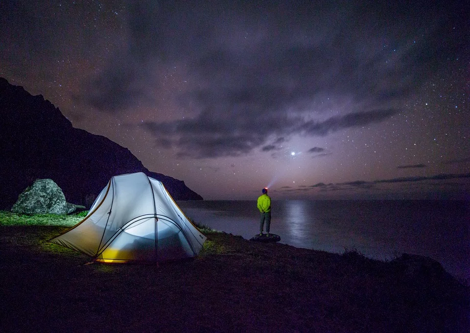 Un hombre en su campamento viendo hacia el cielo estrellado junto al mar. | Foto: Pixabay