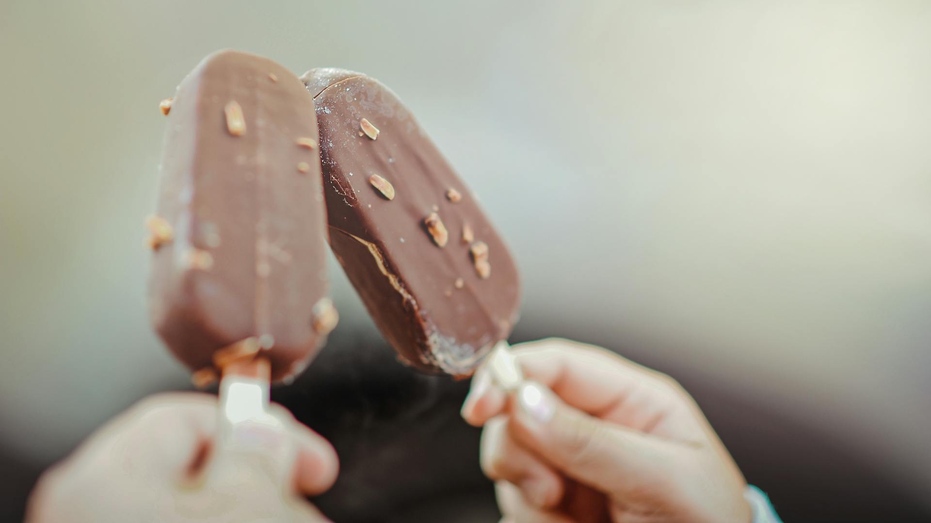 Primer plano de dos manos sujetando palitos de helado de chocolate | Fuente: Pexels