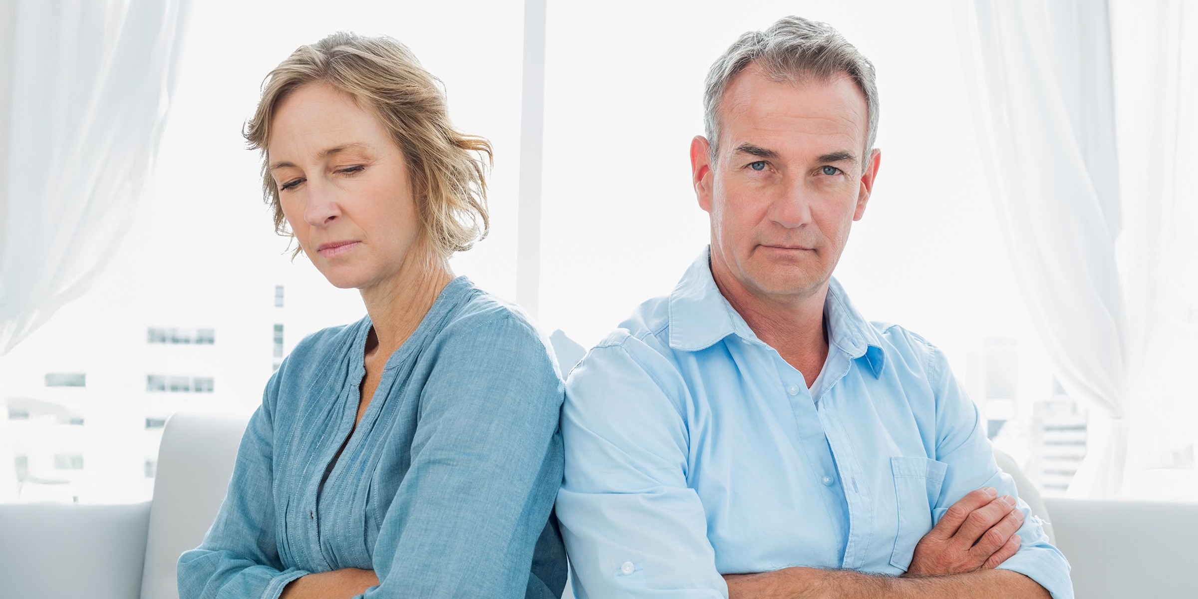 Una tensa pareja de mediana edad sentada con los brazos cruzados | Fuente: Shutterstock