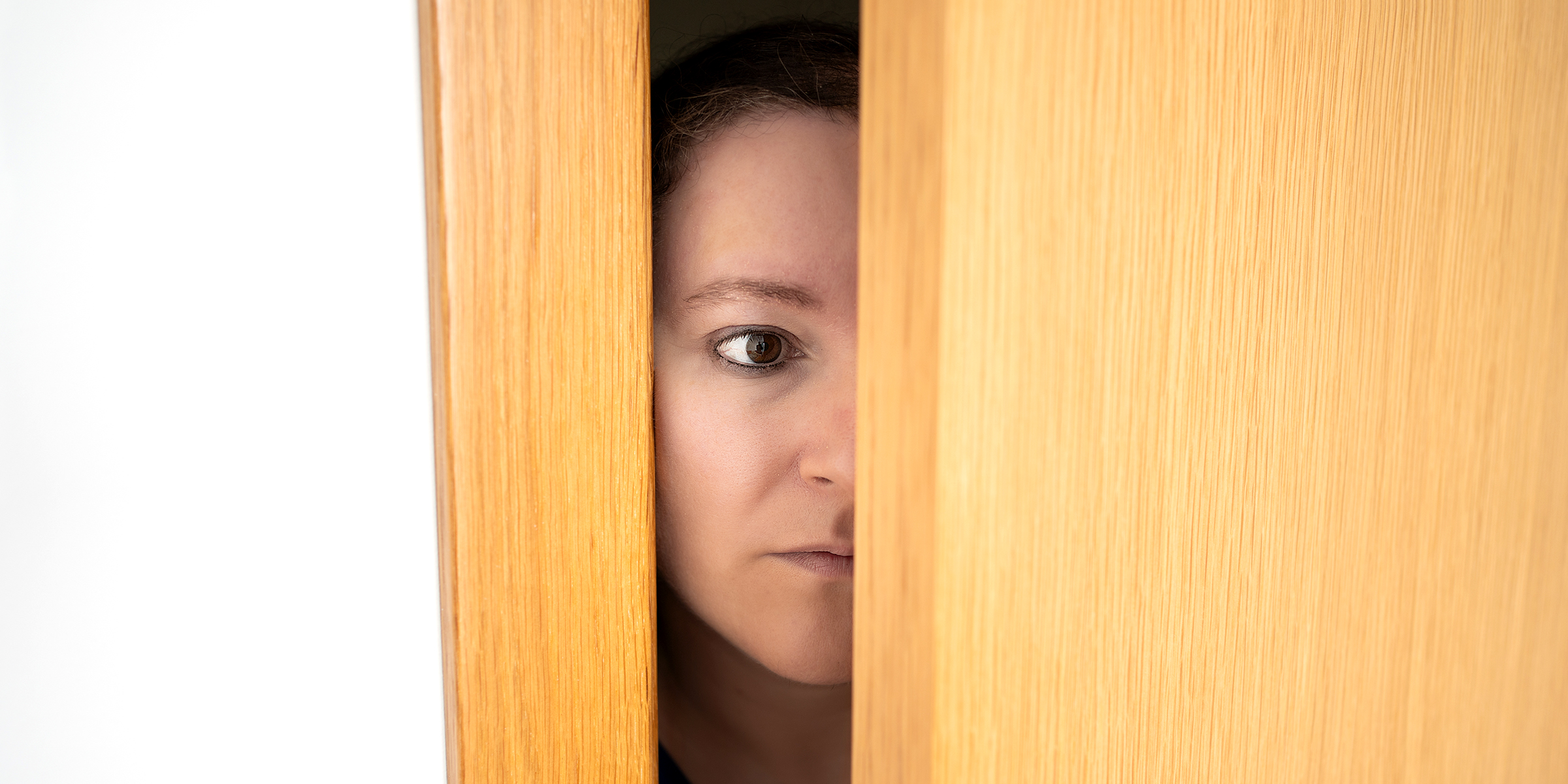 Una mujer sorprendida espiando desde detrás de una puerta | Fuente: Shutterstock