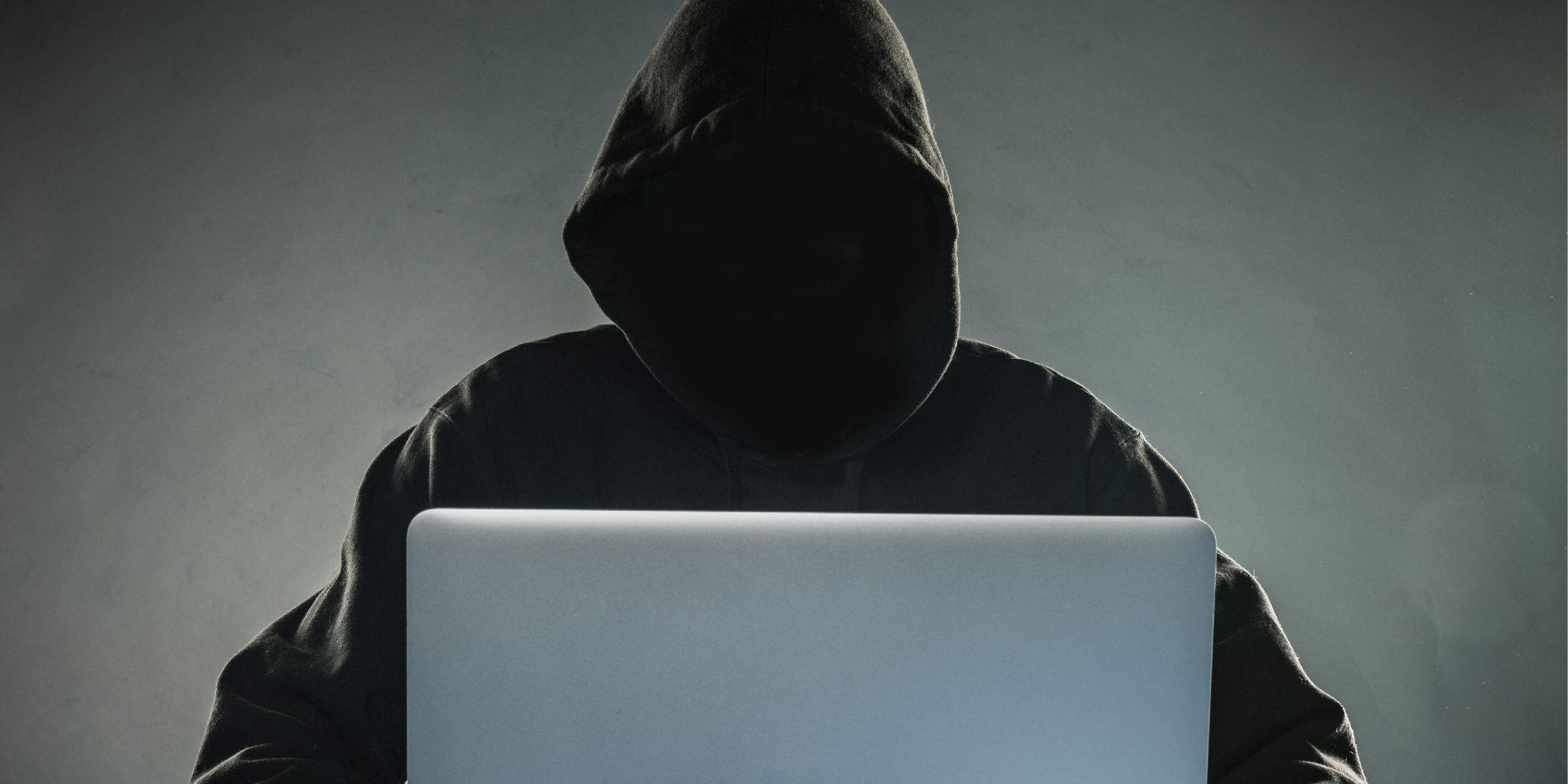 Un hacker con capucha usando un portátil | Fuente: Shutterstock