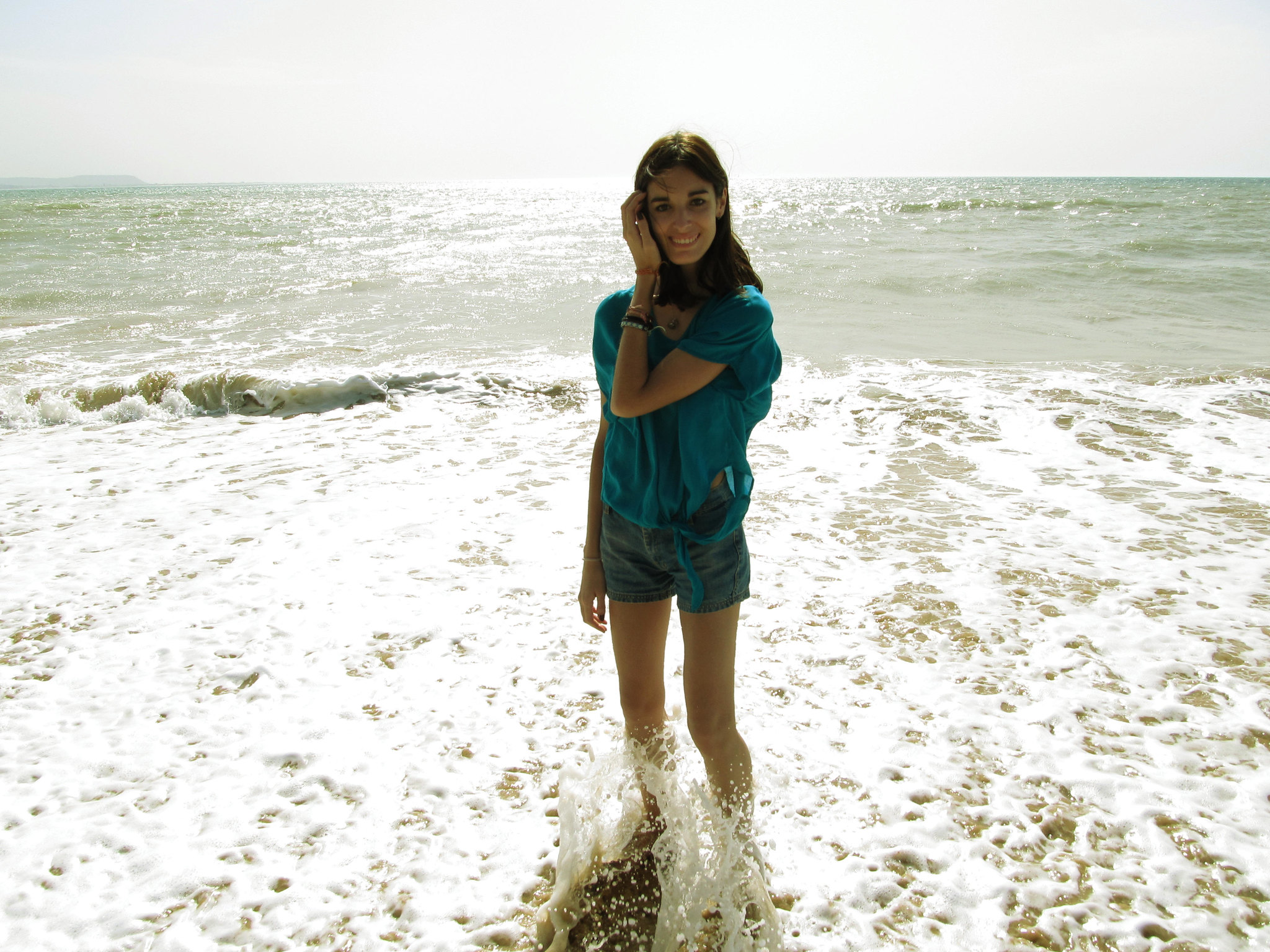 Una joven sonríe de pie en el agua de una playa | Fuente: Flickr