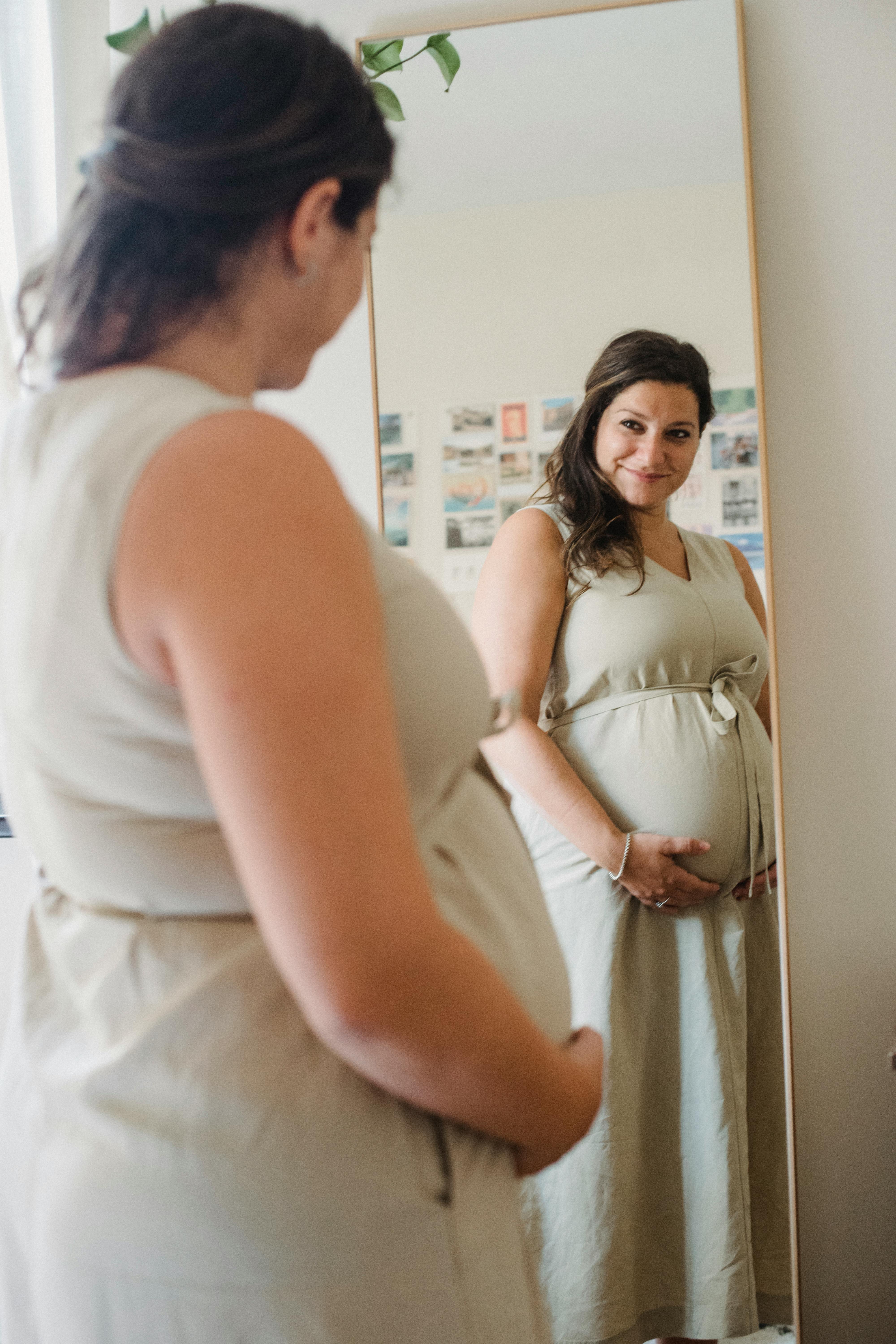 Una embarazada feliz mirándose en un espejo | Fuente: Pexels
