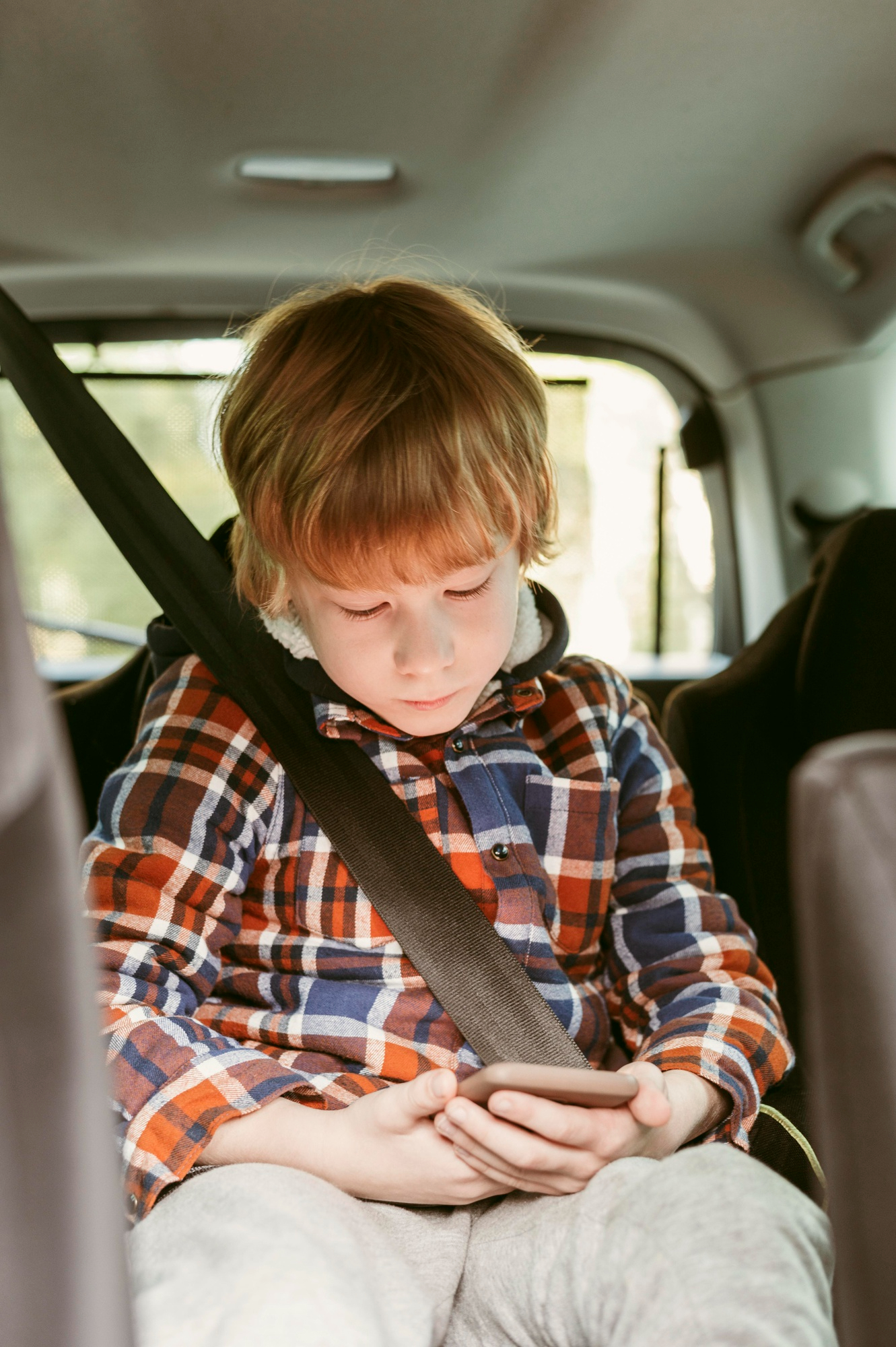 Un niño concentrado en un teléfono en el asiento trasero de un coche | Fuente: Freepik