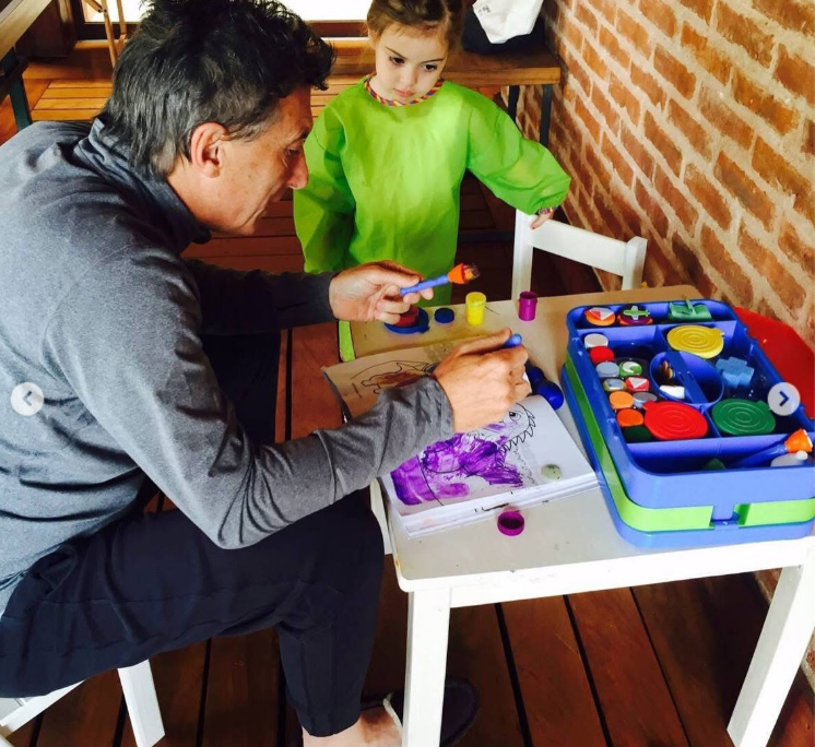 Compartiendo una tarde de juegos y creatividad, Mauricio Macri y Antonia se sientan en una mesa blanca de madera. Mientras él pinta con un pincel en un cuaderno de dibujos, la niña, con un delantal verde manzana para manualidades, observa de pie junto a una colorida caja de témperas y sellos. | Fuente: Instagram/mauriciomacri