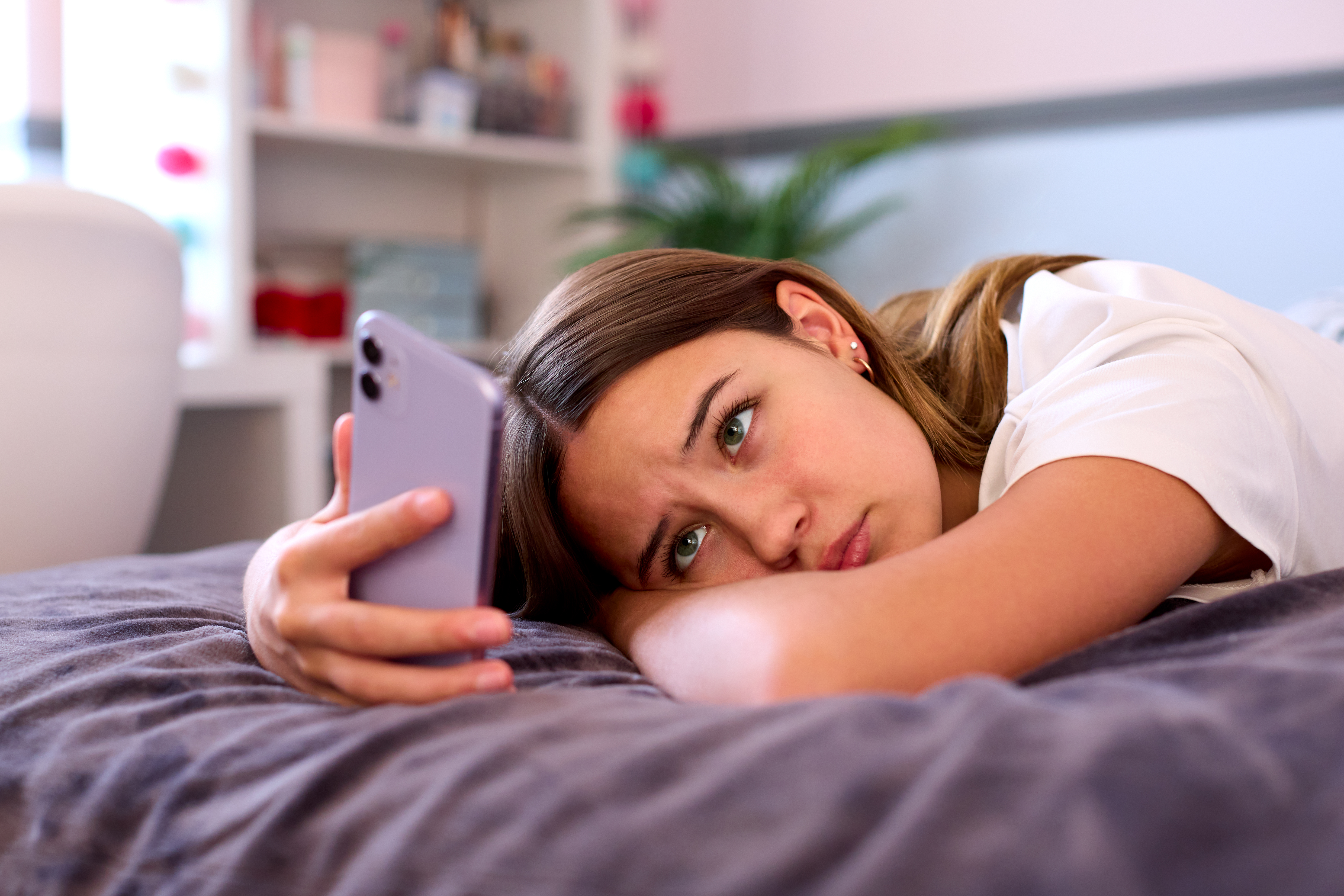 Adolescente deprimida tumbada en la cama de su casa mirando el móvil | Foto: Getty Images