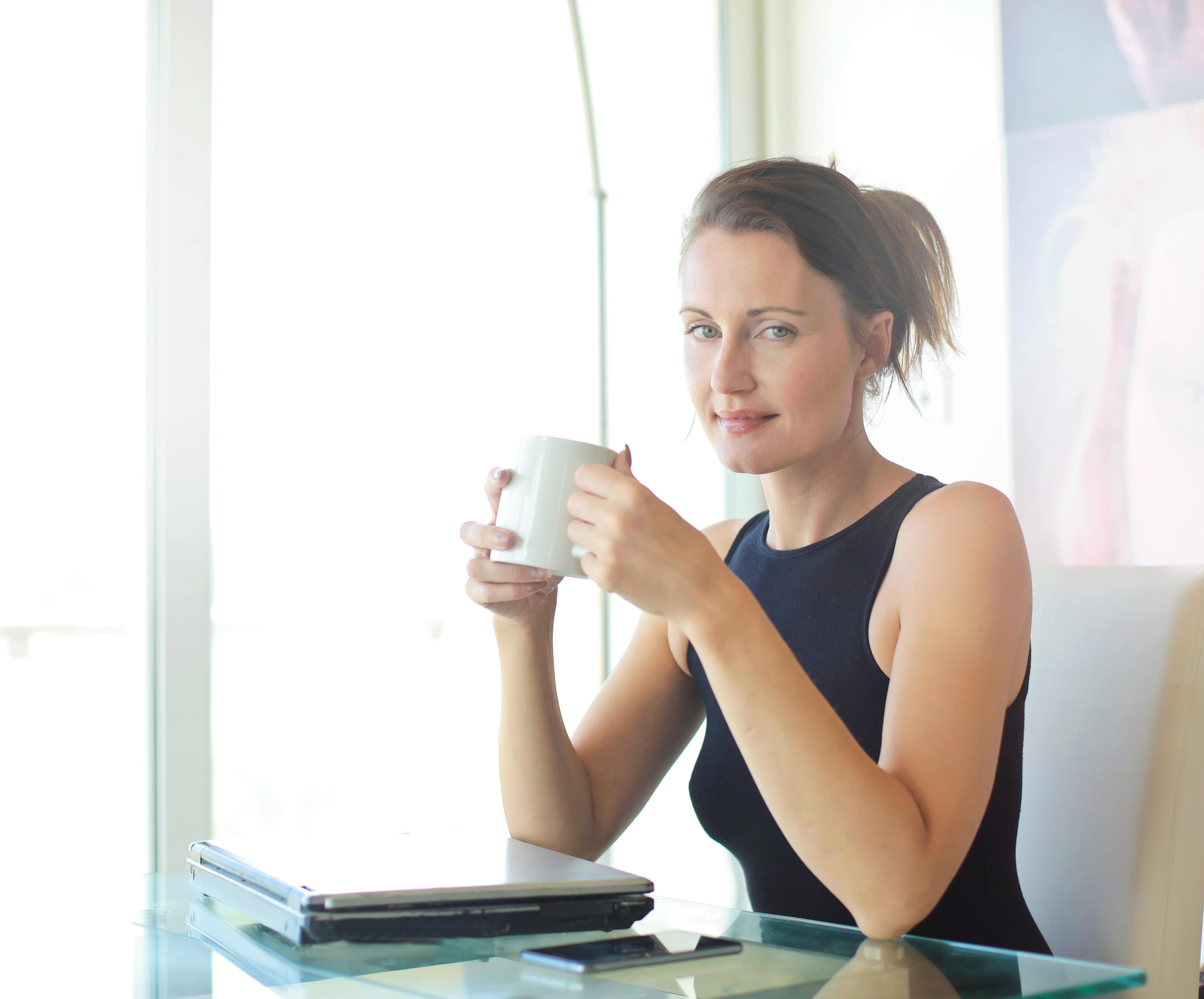 A woman in a black tank top holding a white ceramic mug. | Source: Pexels
