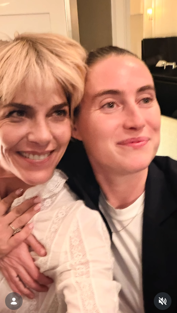 Selma Blair y un acompañante sonríen con calidez uno al lado del otro en un primer plano tomado en un interior el 11 de octubre de 2026. Blair luce una blusa de encaje marfil transparente con un diseño muy elaborado y delicados bordados, con una mano apoyada sobre el pecho mientras se inclinan juntos. | Fuente: Instagram/selmablair