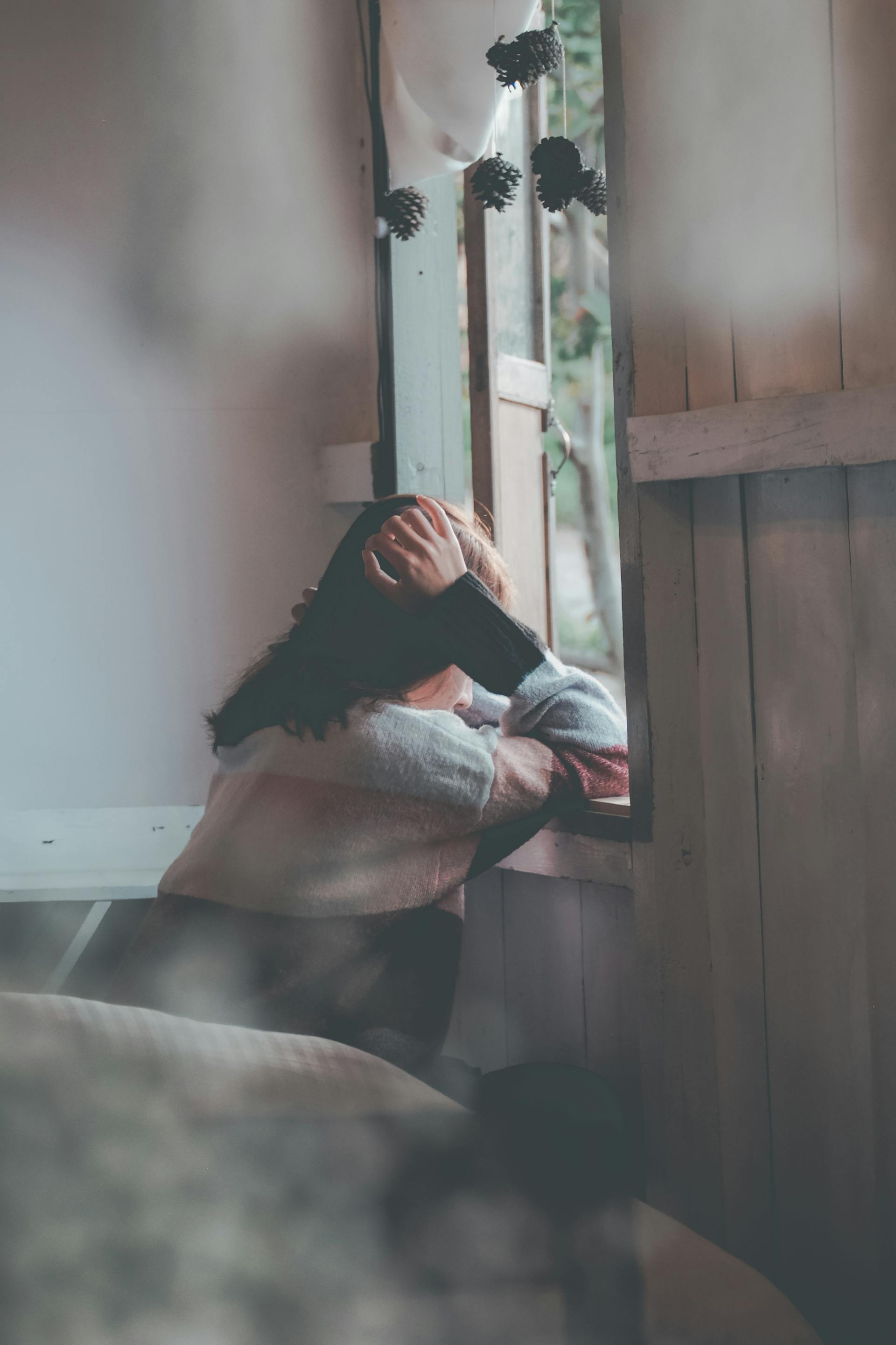 Una mujer apoyada en el alféizar de una ventana y mirando al exterior | Fuente: Pexels