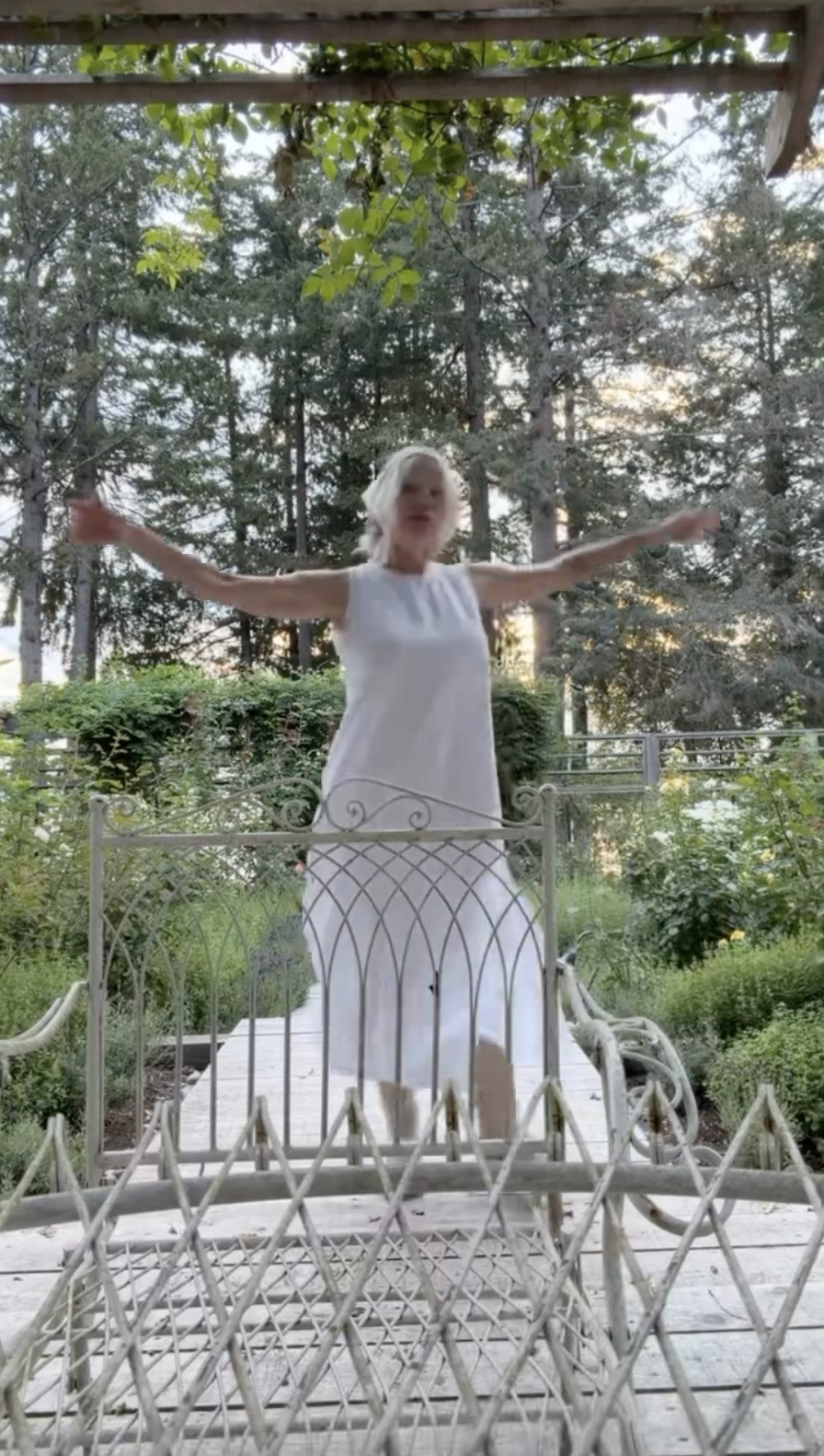 Pamela Anderson da vueltas libremente con los brazos extendidos por la terraza de madera de su jardín de Arcady, reflejando a la perfección su filosofía personal de "vivir con romanticismo estés donde estés". Con un vestido blanco sin mangas de largo medio, ligero y vaporoso, y con un exuberante telón de fondo de árboles de hoja perenne y la vegetación del jardín, captura esa paz desenfadada y ese romanticismo creado por ella misma que definen su tranquila vida en la isla de Vancouver. | Fuente: Instagram/pamelaanderson