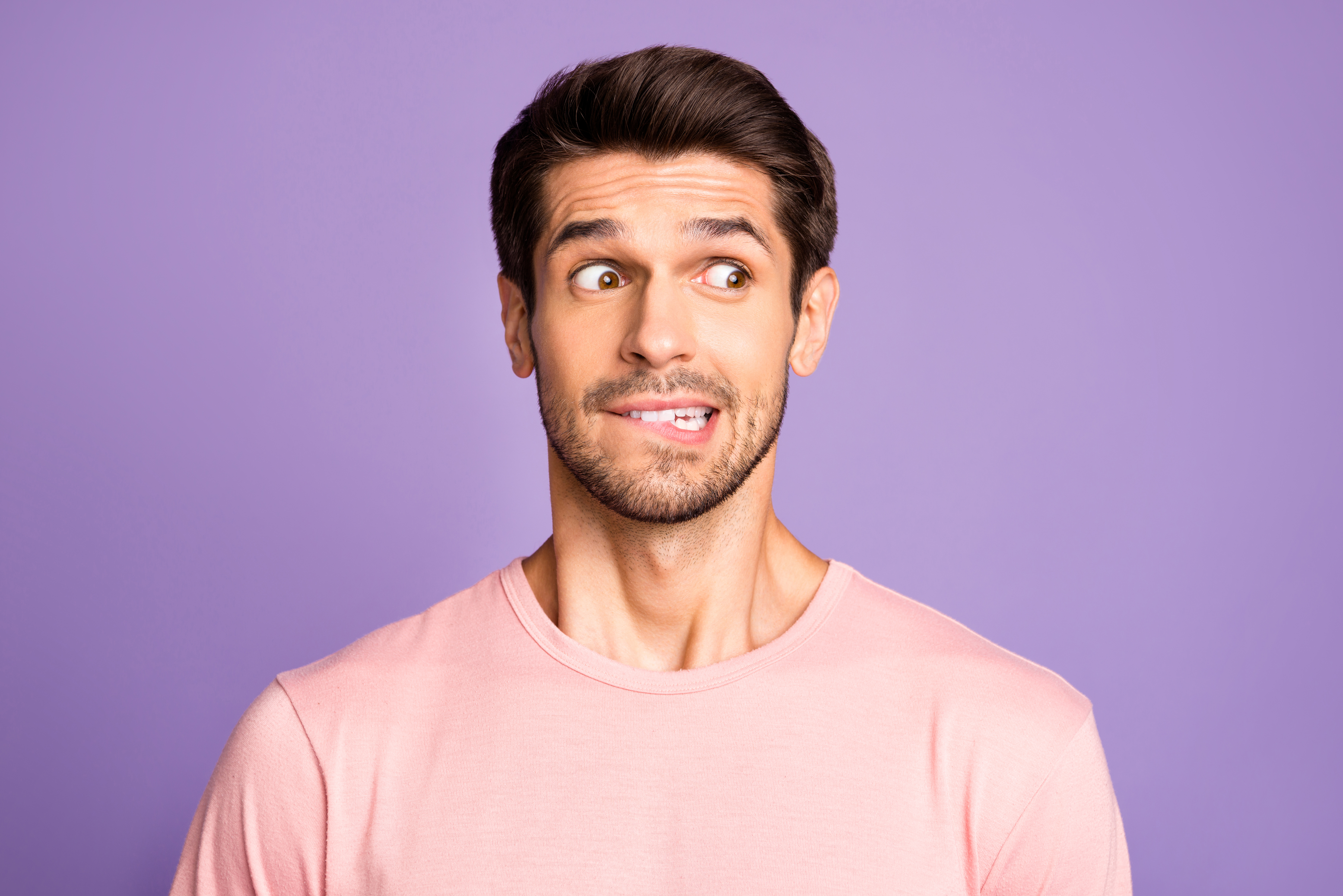 Retrato en primer plano de su él agradable atractivo divertido confundido moreno barbudo con camiseta rosa esperando noticias mordiéndose el labio aislado sobre fondo violeta púrpura lila color pastel | Foto: Getty Images