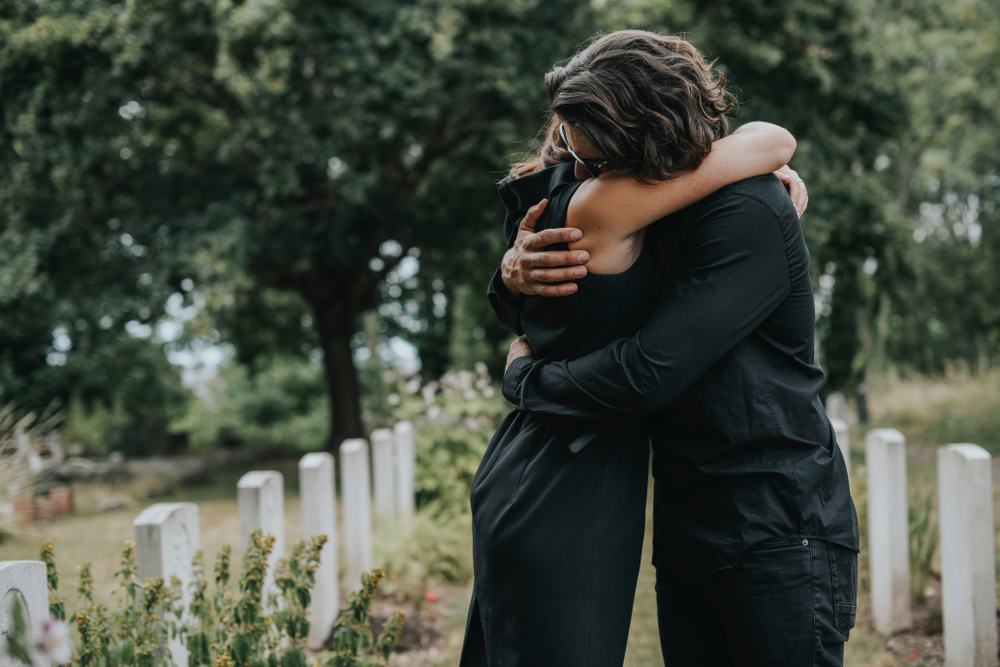 Hombre intentando consolar a una mujer en un cementerio. | Fuente: Shutterstock