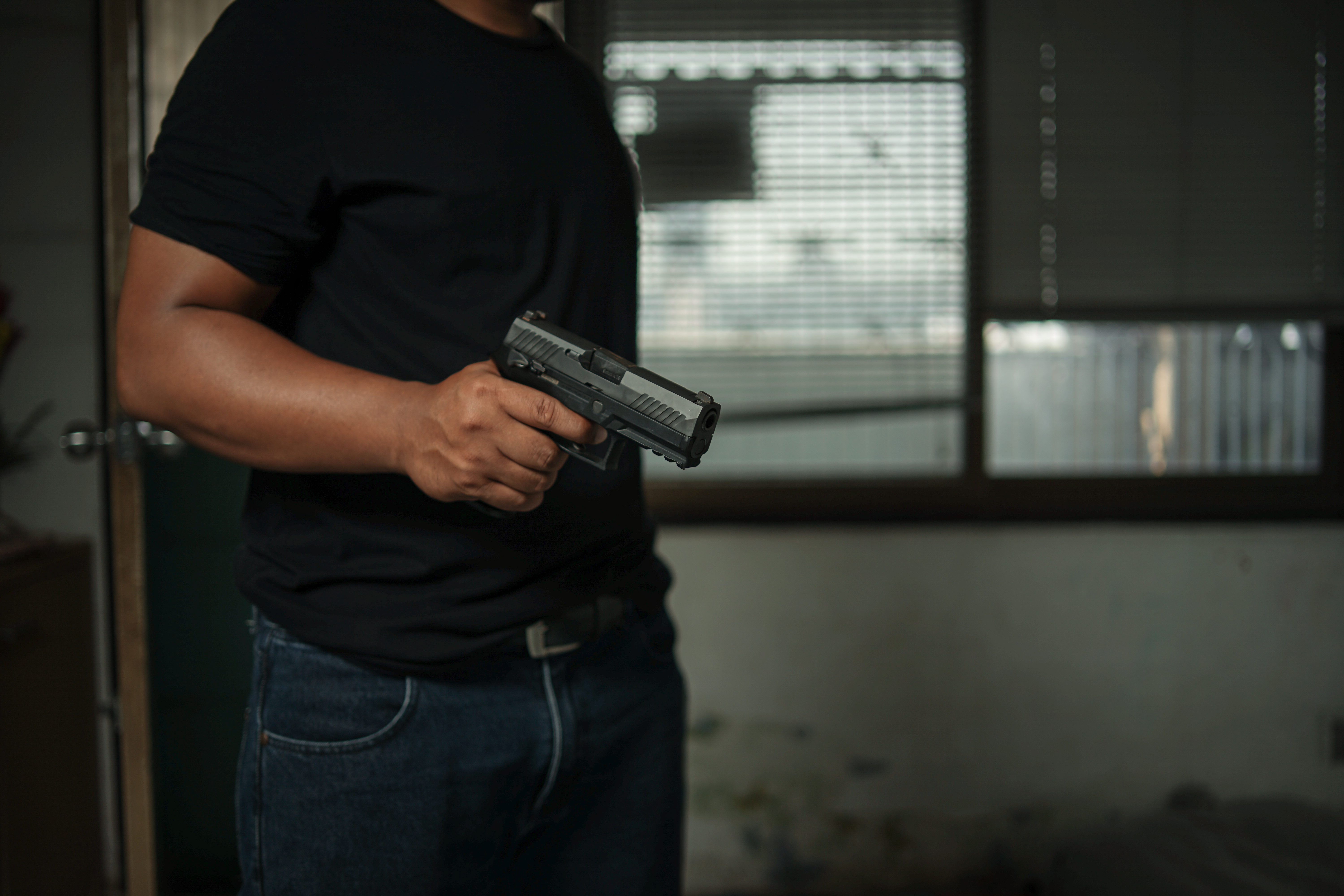 Hombre con una pistola en la mano, de pie en una habitación vestida de negro, apuntando y apuntando a un objetivo | Fuente: Shutterstock.com