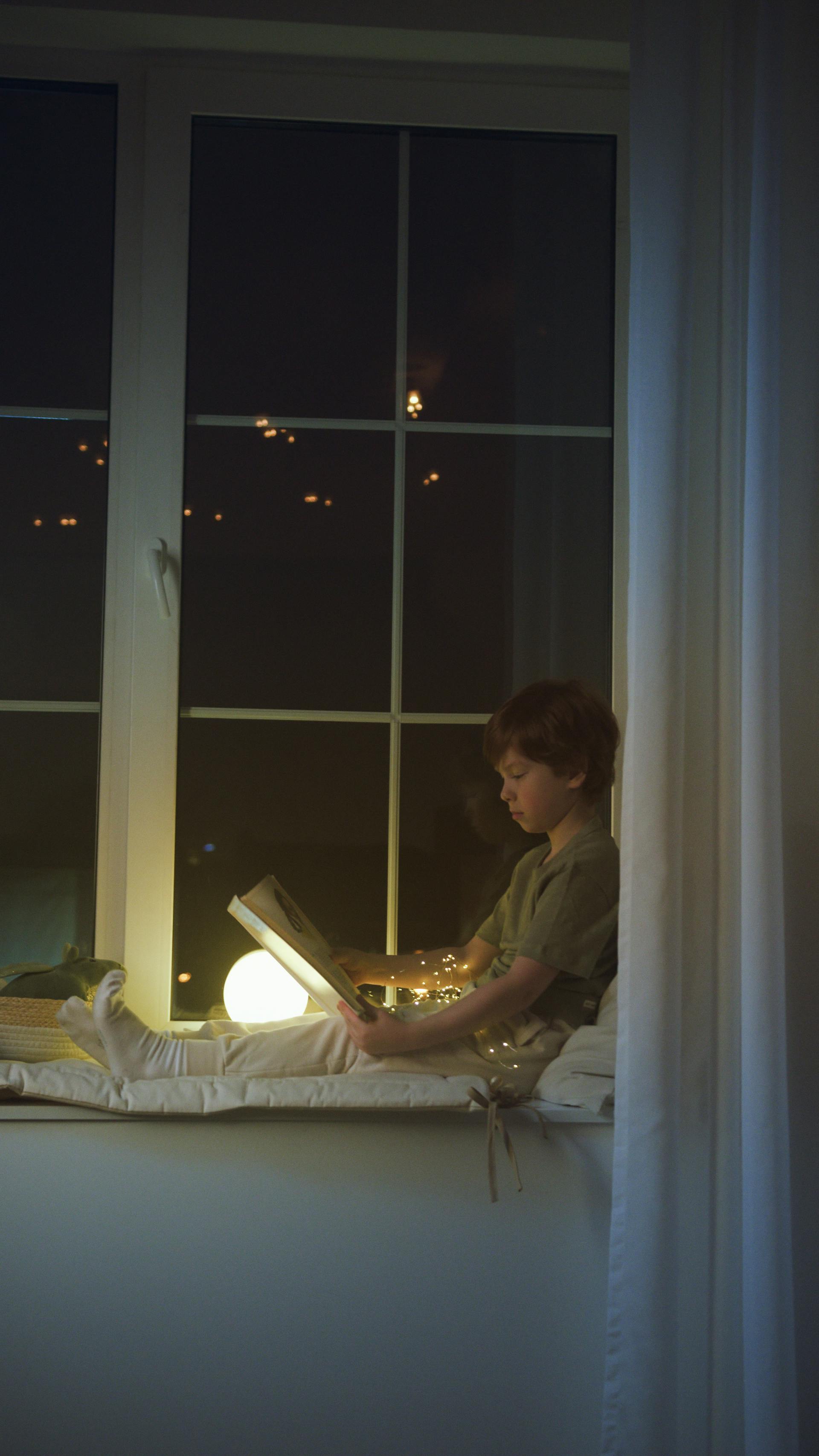 Un niño leyendo un libro sentado en el alféizar de una ventana | Foto: Pexels