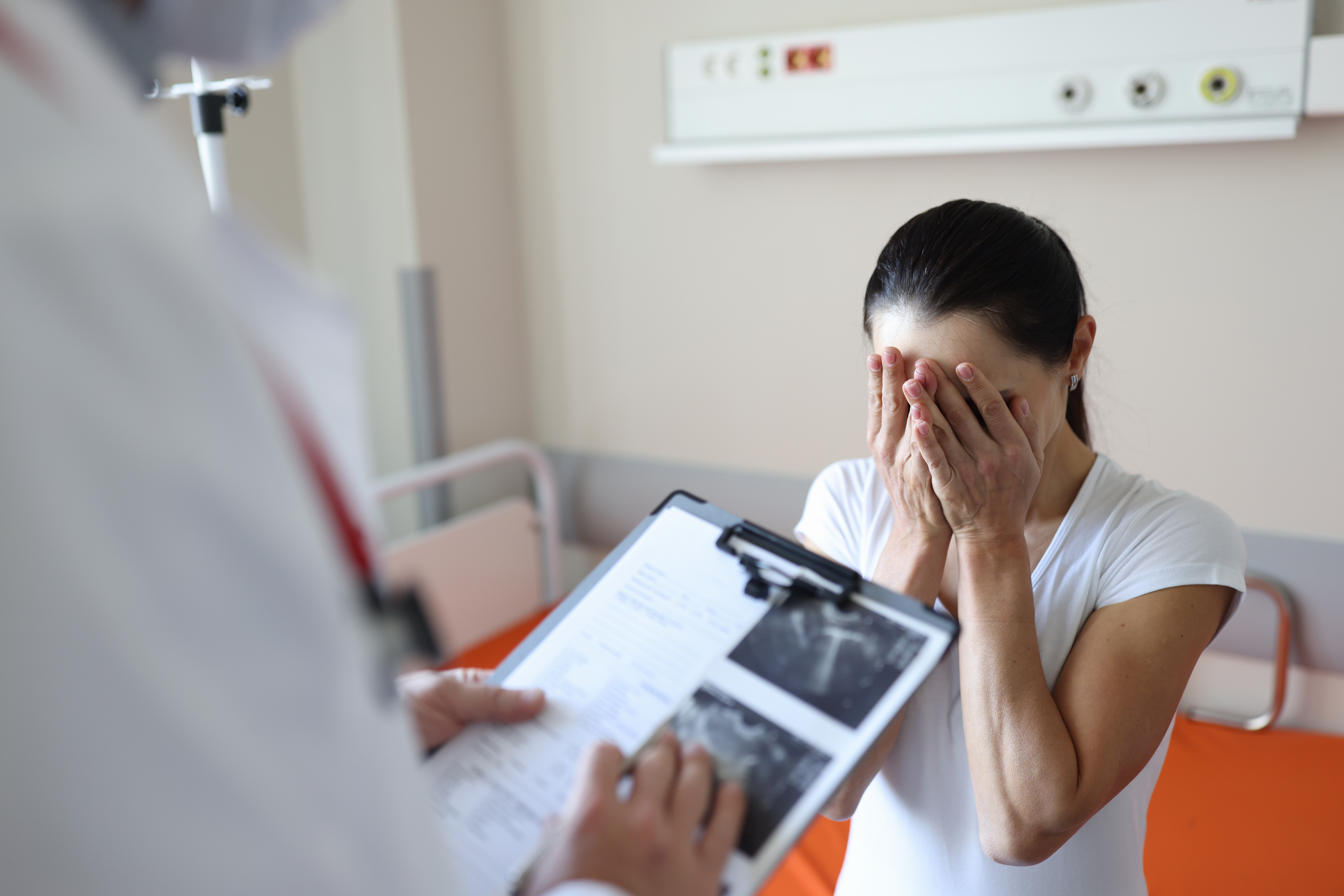 Médico sosteniendo documentos delante de una mujer que llora en una clínica. | Fuente: Shutterstock