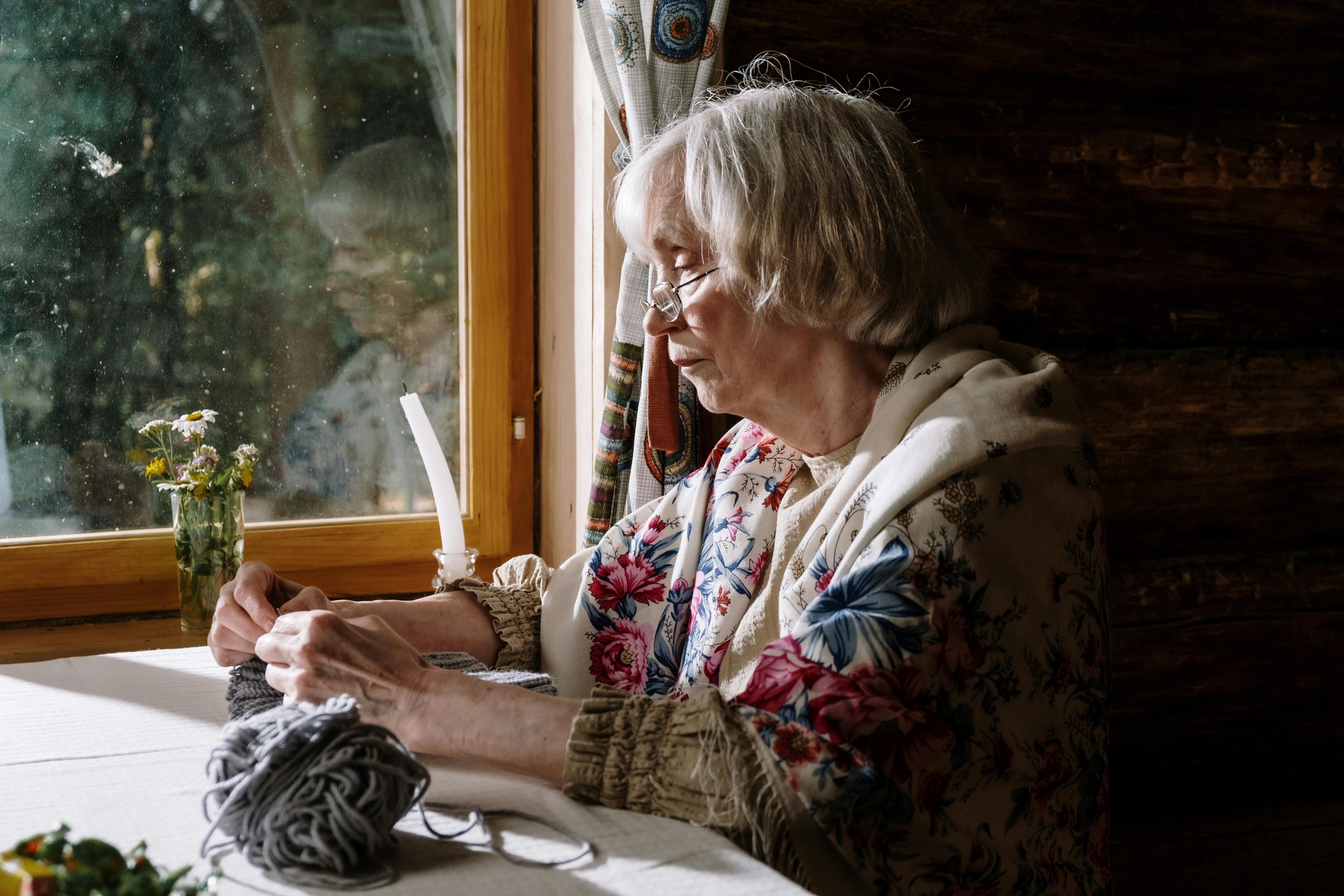 Abuela tejiendo junto a la ventana, orgullosa y contenta | Fuente: Pexels