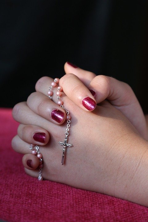 Mujer joven orando con un rosario entre sus manos. | Imagen: Pixabay